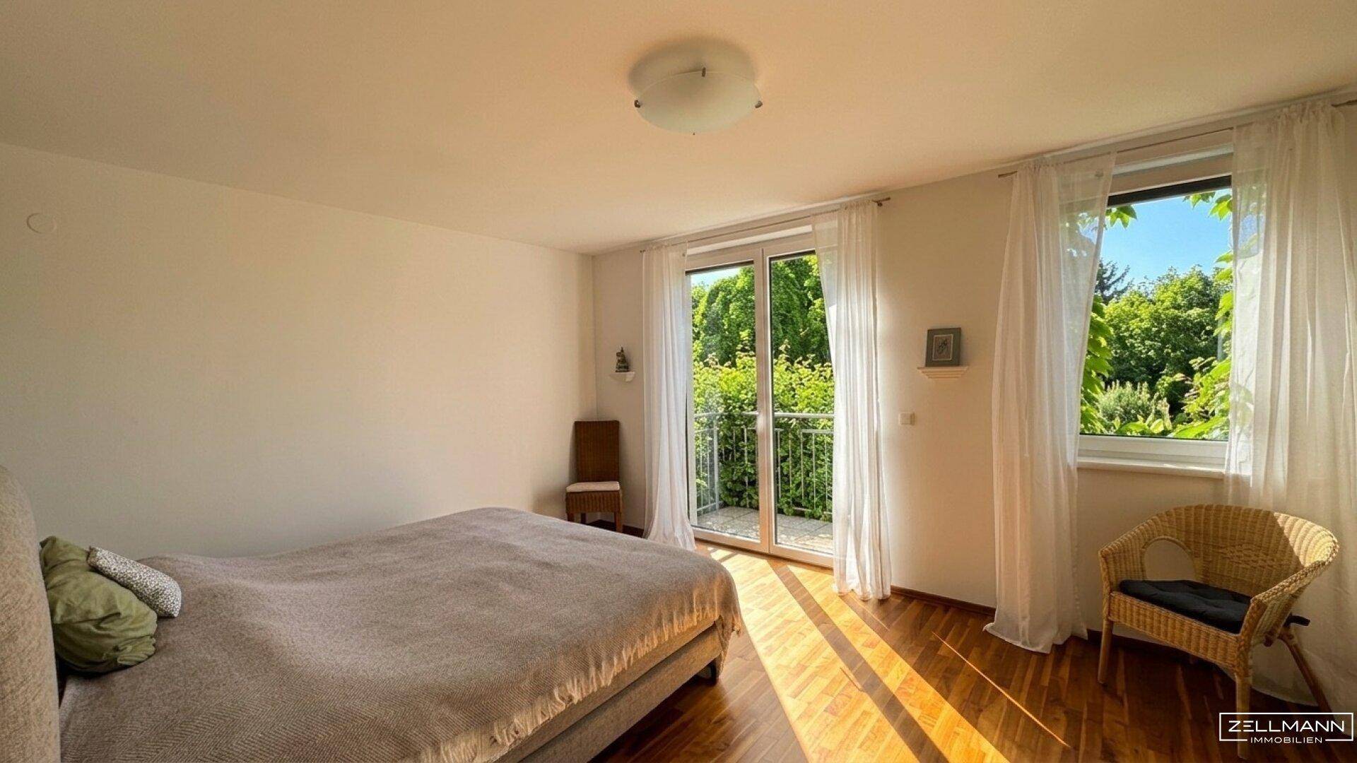 Helles Schlafzimmer mit Holzboden, großem Bett und Zugang zu einem französischen Balkon.