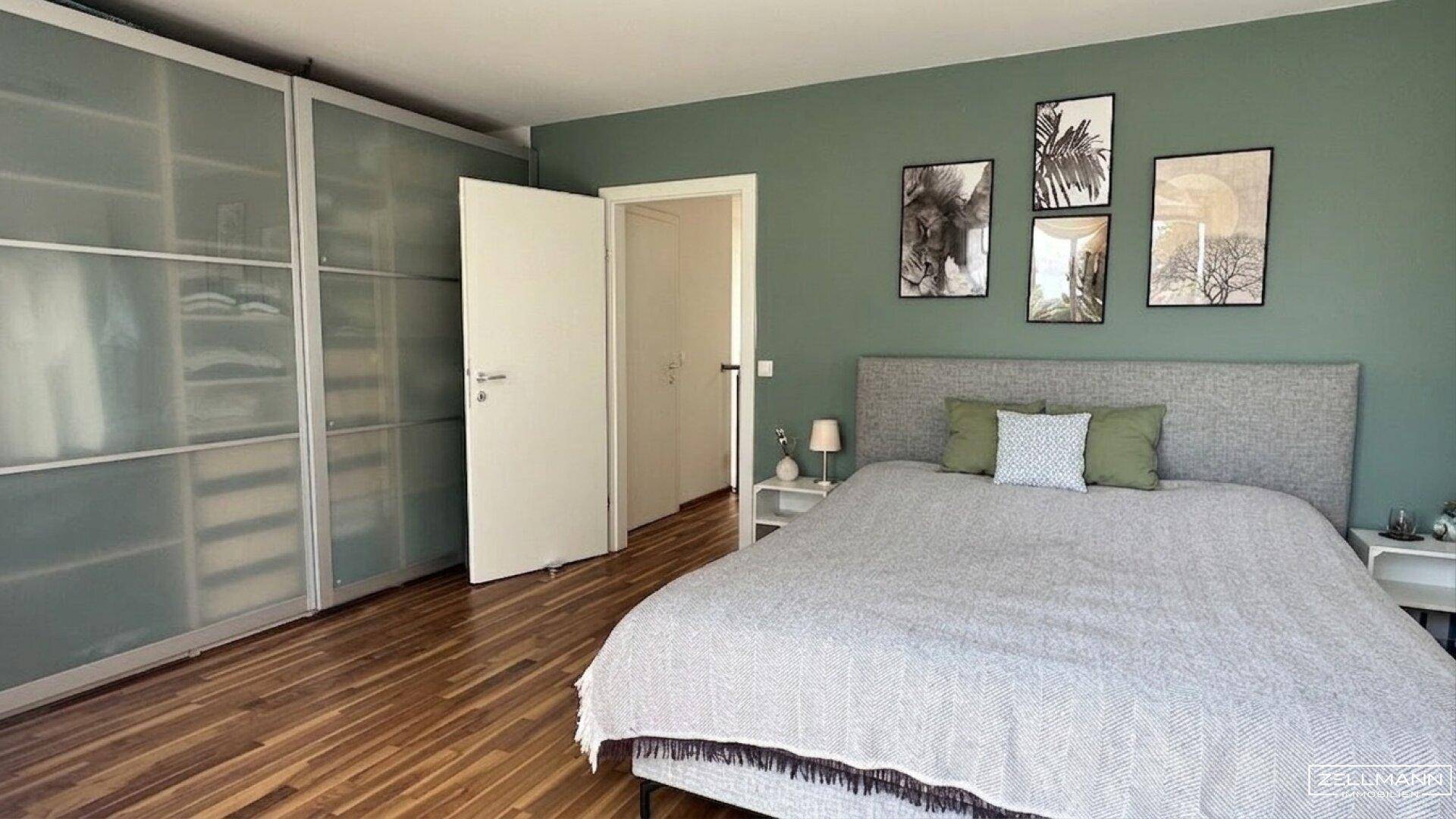 Geräumiges Schlafzimmer mit Holzboden, grüner Wand und integrierten Kleiderschränken.