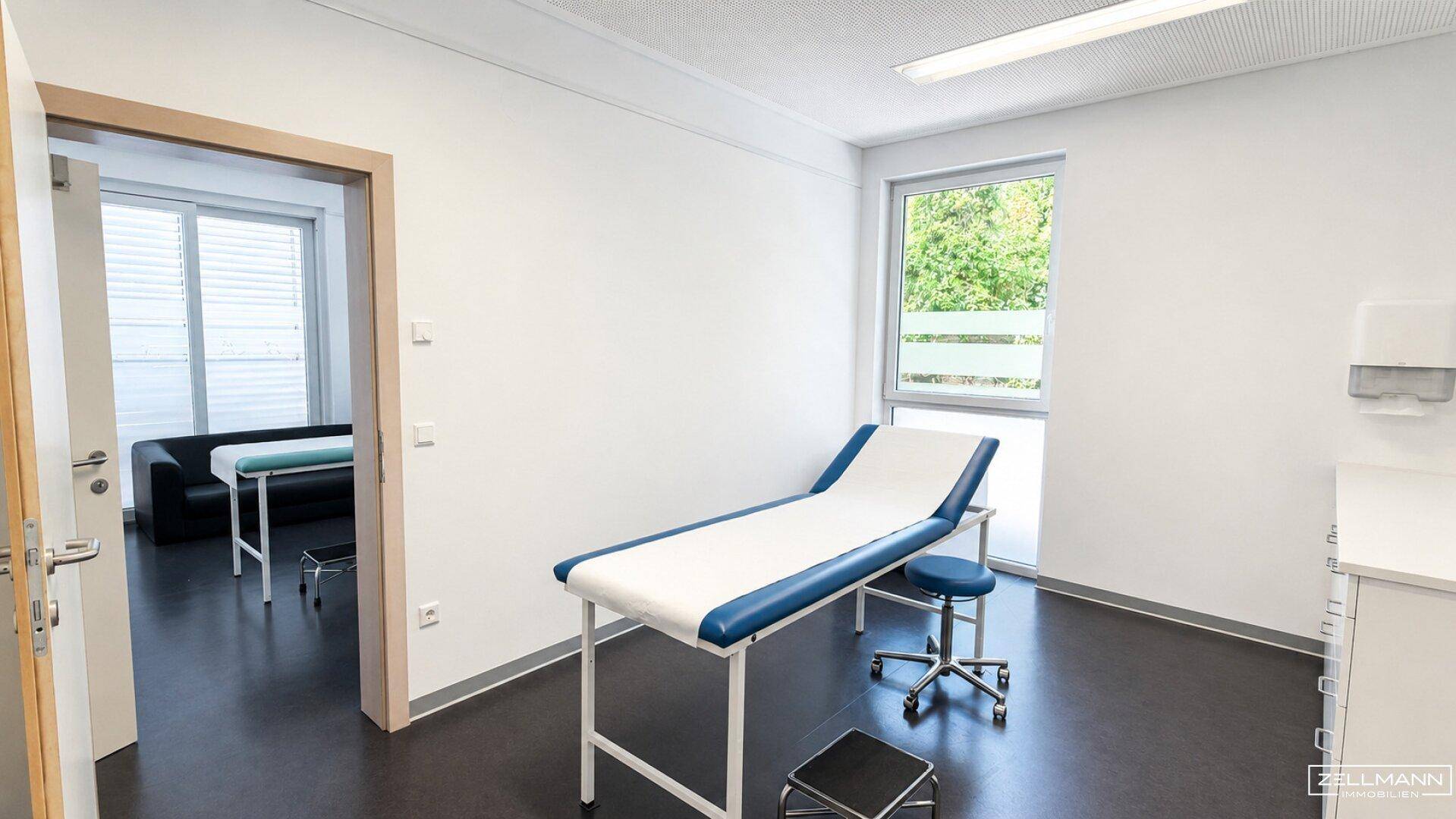Helles Behandlungszimmer mit Untersuchungsliege und Fensterblick ins Grüne.