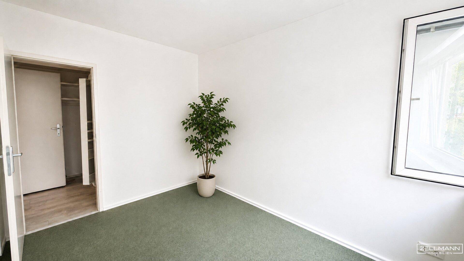 Helles Schlafzimmer mit grünem Teppichboden und Blick ins Grüne durch das Fenster.