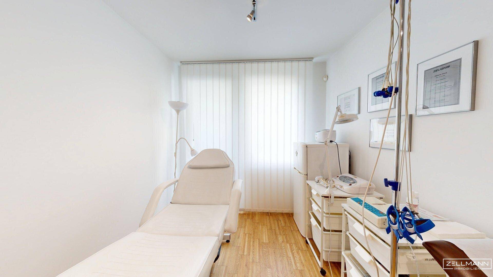 Kleineres Behandlungszimmer mit Untersuchungsliege, medizinischen Geräten und Fenster für Tageslicht.
