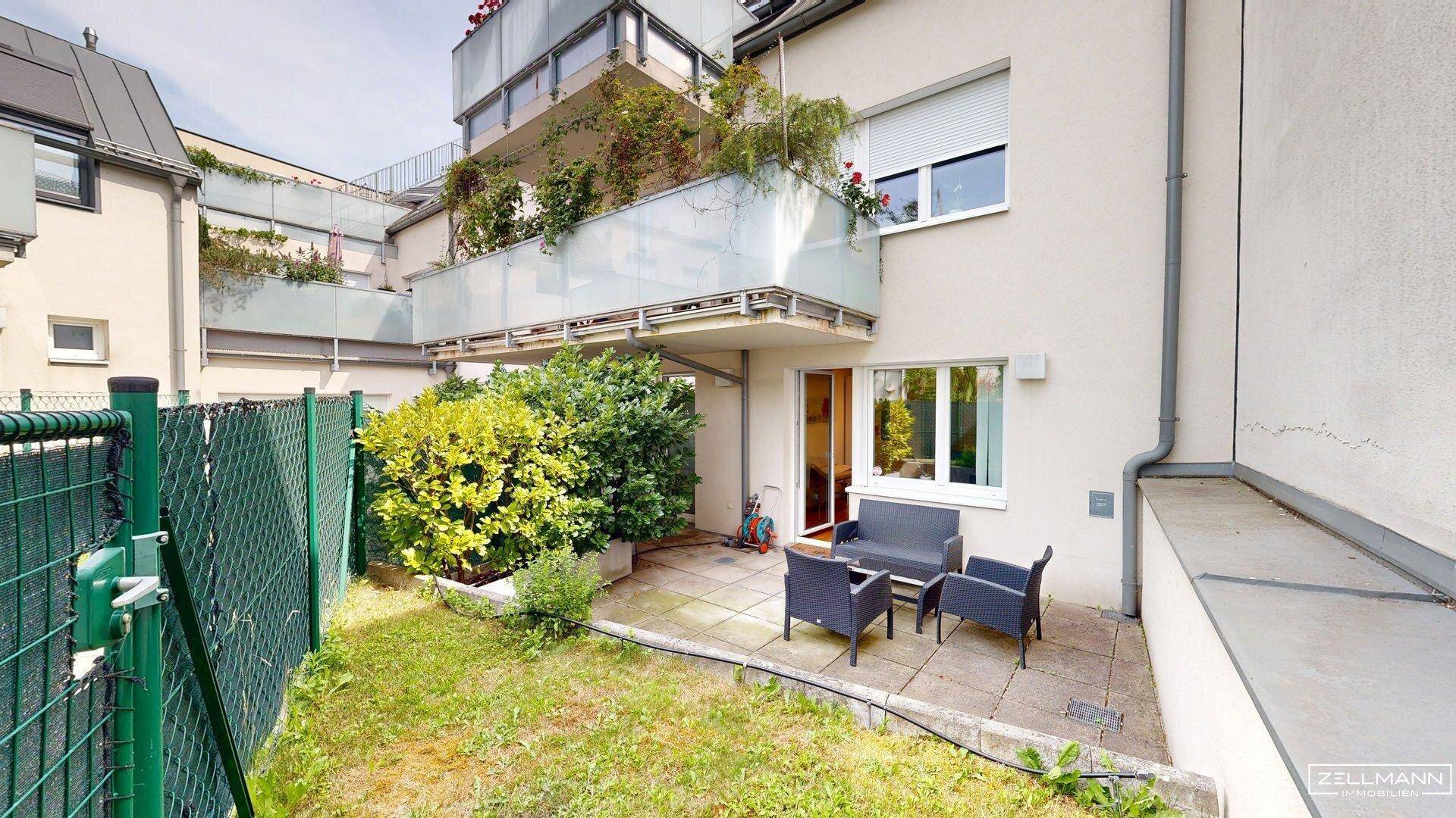 Außenbereich mit kleiner Rasenfläche, gepflasterter Terrasse und Sitzgelegenheiten vor dem Gebäude.