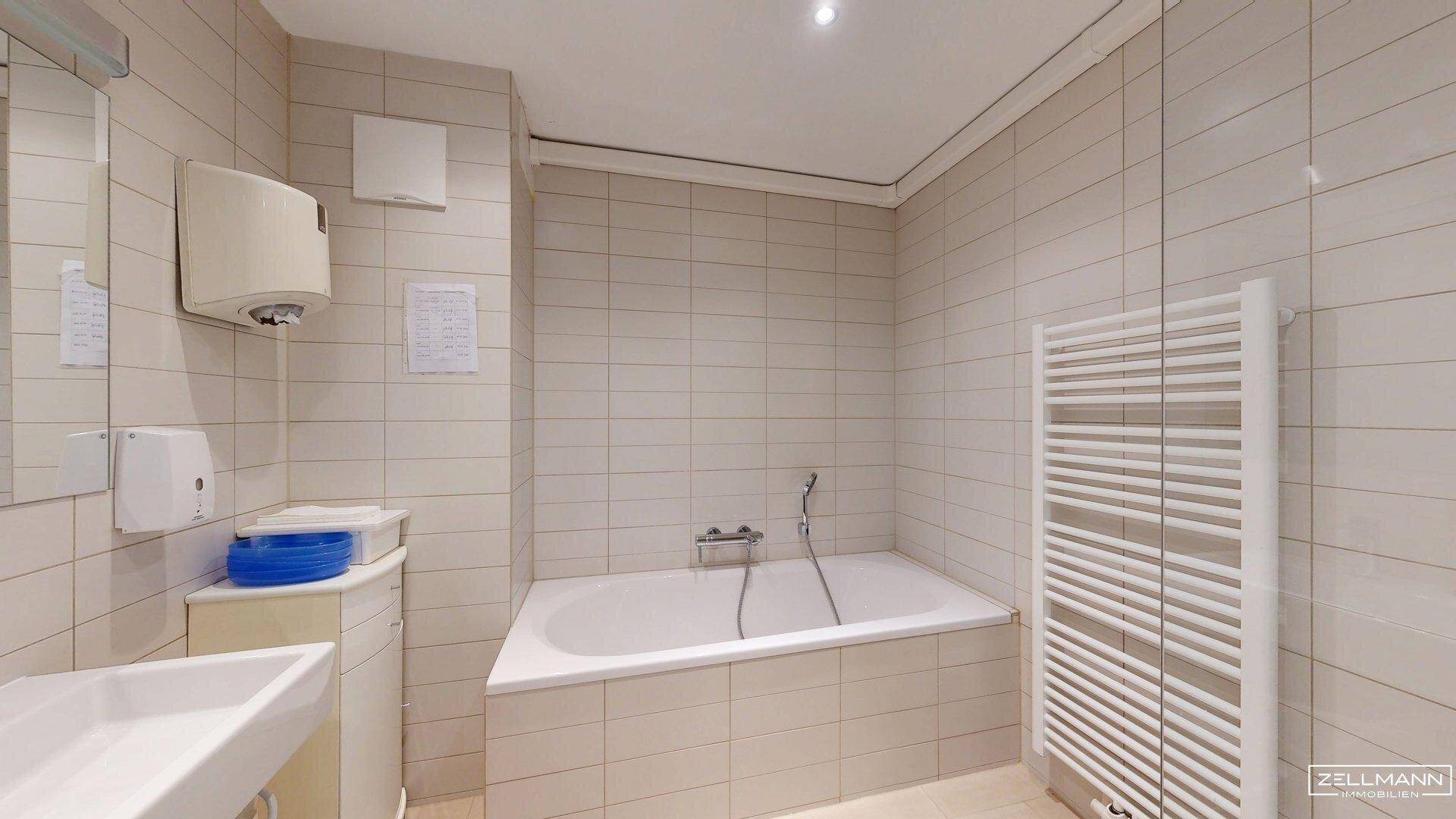 Badezimmer mit Badewanne, Waschbecken und hellen Fliesen an Wänden und Boden.