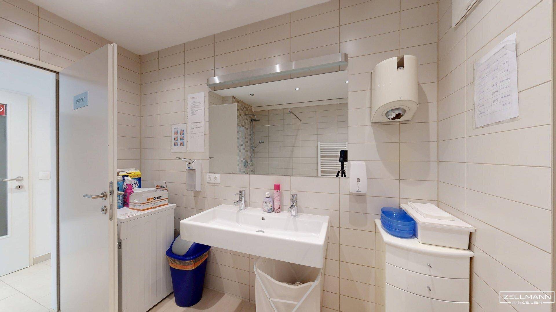 Badezimmer mit Waschbecken, großem Spiegel und hellen Fliesen an den Wänden.