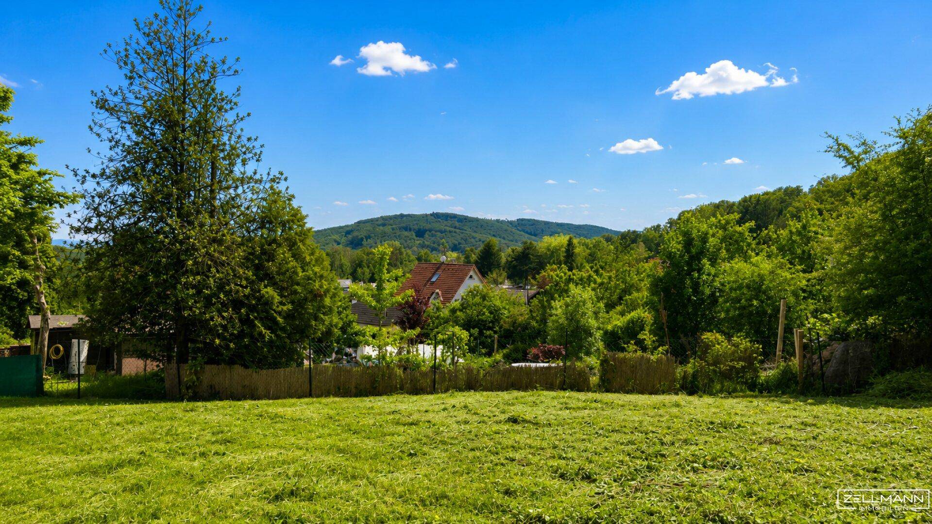 Weitläufiges grünes Grundstück mit Blick auf ein Haus, Bäume und sanfte Hügel.