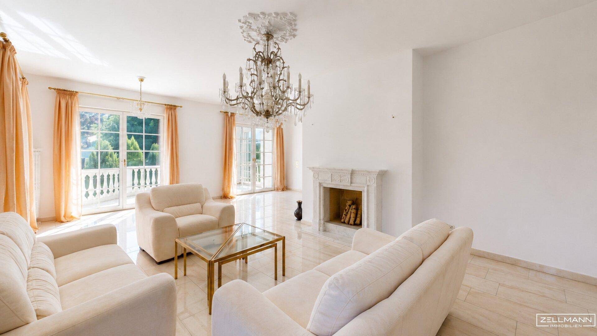 Helles Wohnzimmer mit elegantem Kronleuchter, dekorativem Kamin und Zugang zu einem Balkon.