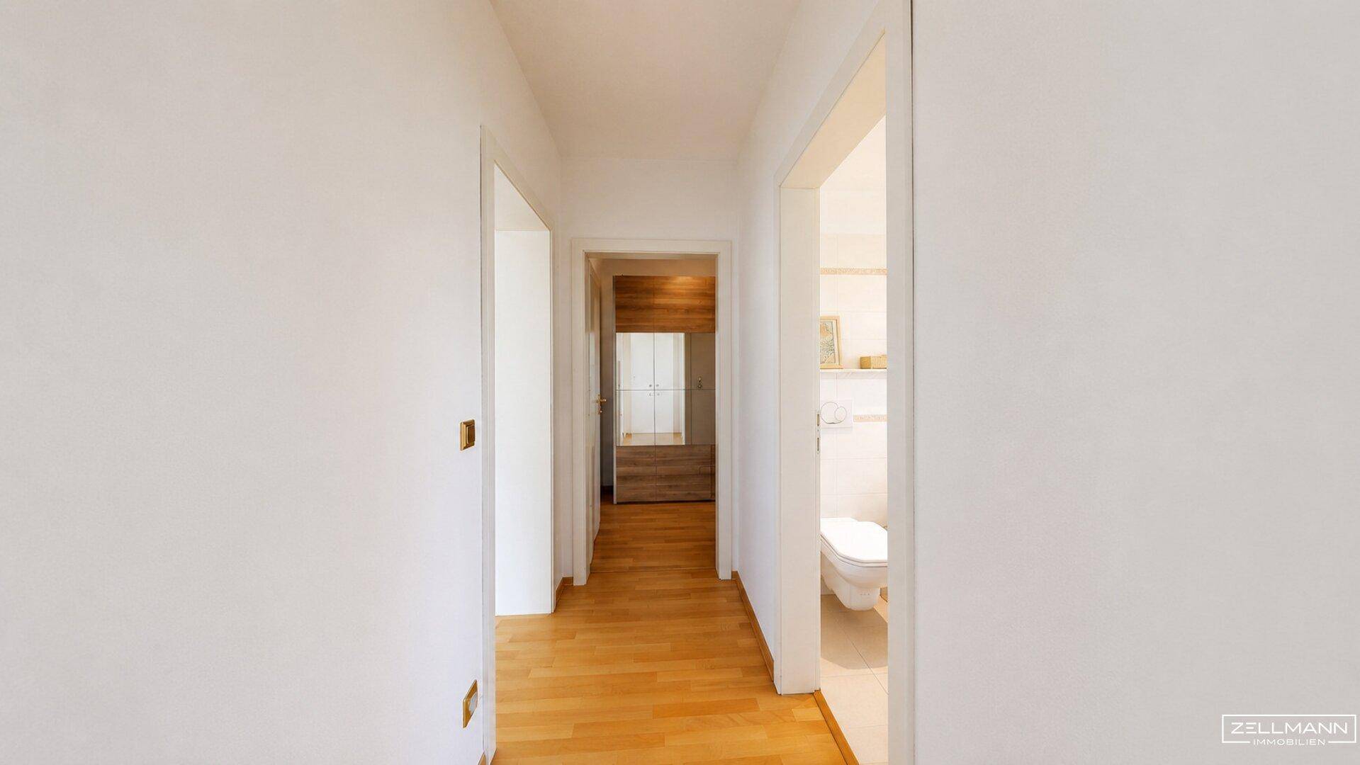 Heller Flur mit Holzfußboden, weißen Wänden und Zugang zu verschiedenen Zimmern.