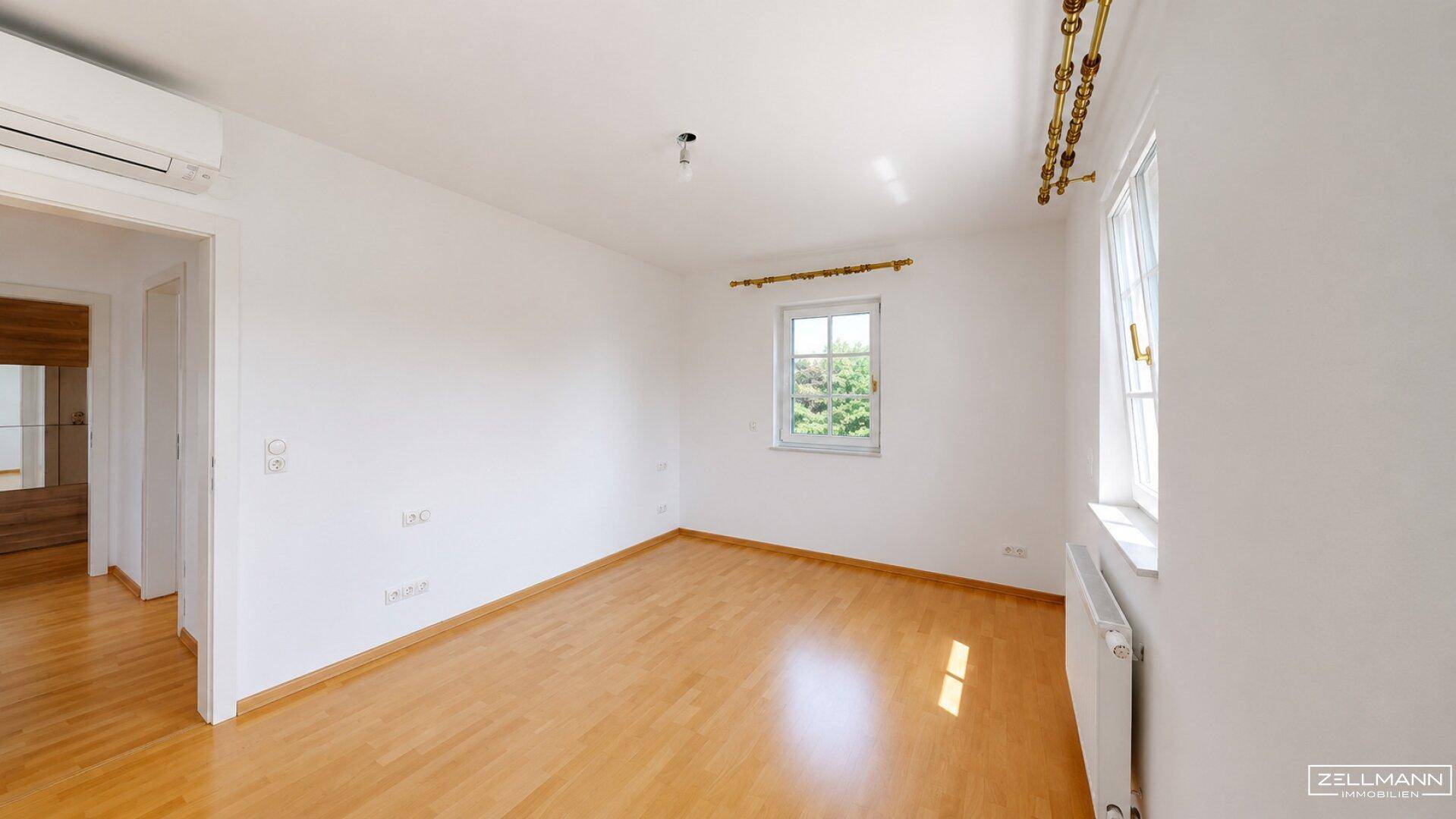 Geräumiges Zimmer mit hellem Holzfußboden, Klimaanlage und zwei Fenstern für viel Tageslicht.