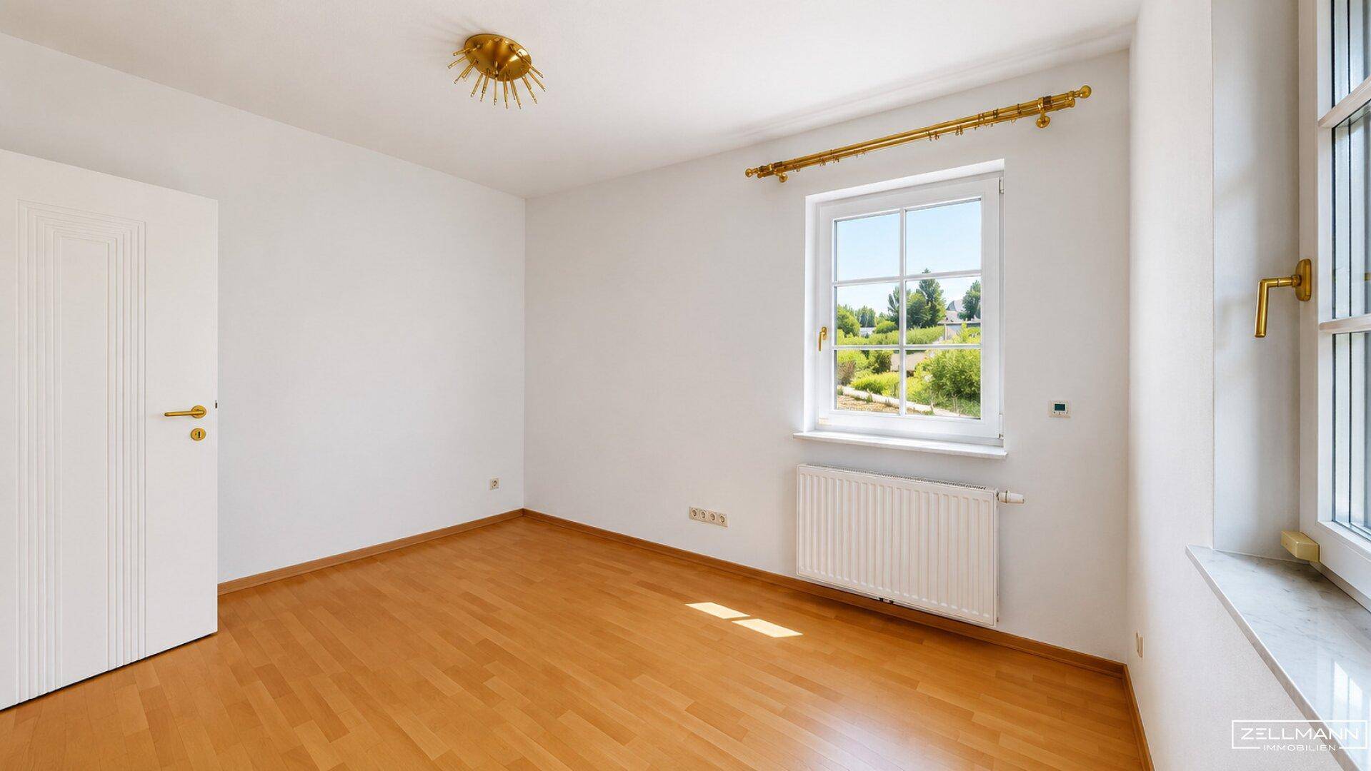 Helles Zimmer mit Holzfußboden, weißen Wänden und Fenster mit weitem Blick ins Grüne.