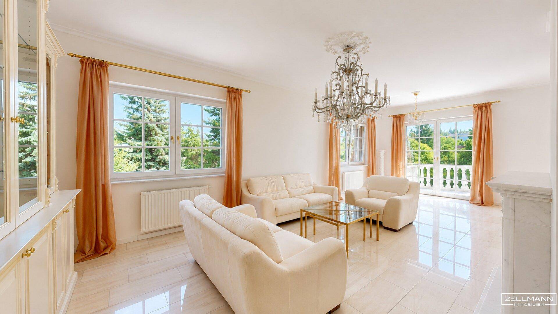 Helles Wohnzimmer mit bequemen Sofas, Fliesenboden und großen Fenstern mit Grünblick.