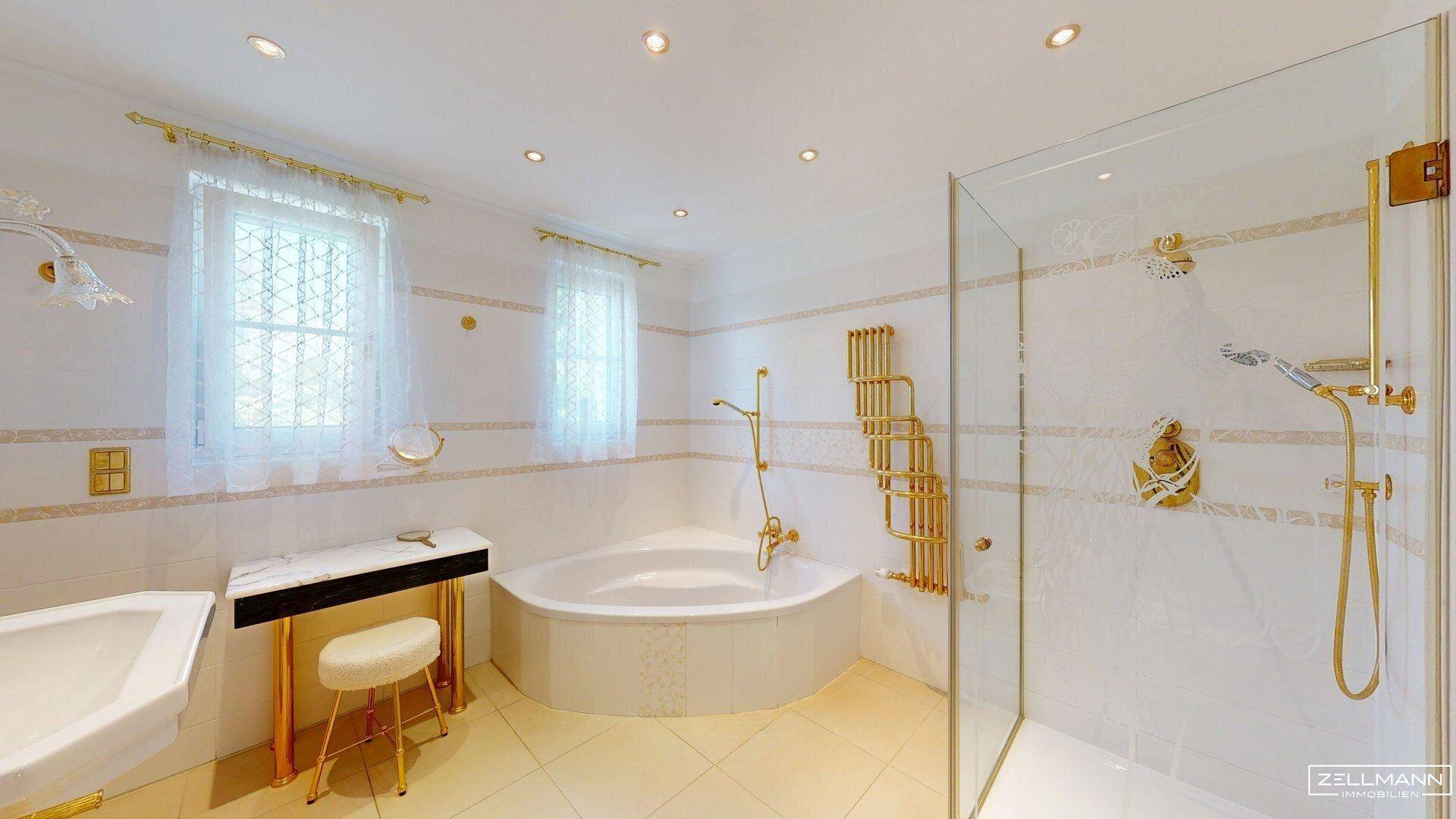 Luxuriöses Badezimmer mit Eckbadewanne, Glasdusche, Waschtisch und goldenen Armaturen.