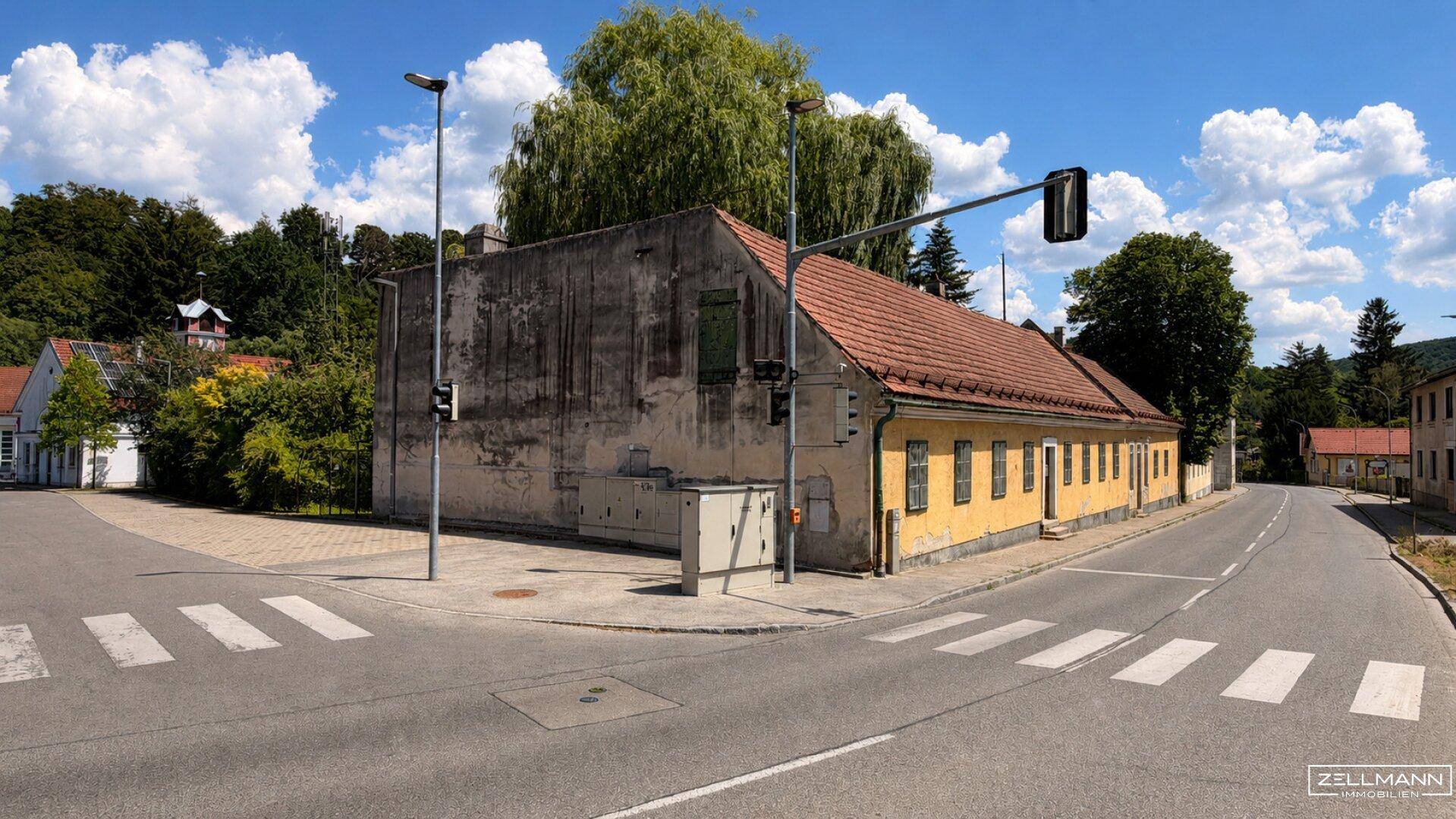 Straßenansicht der beiden Gebäude an einer Kreuzung mit Ampel und Zebrastreifen unter blauem Himmel.