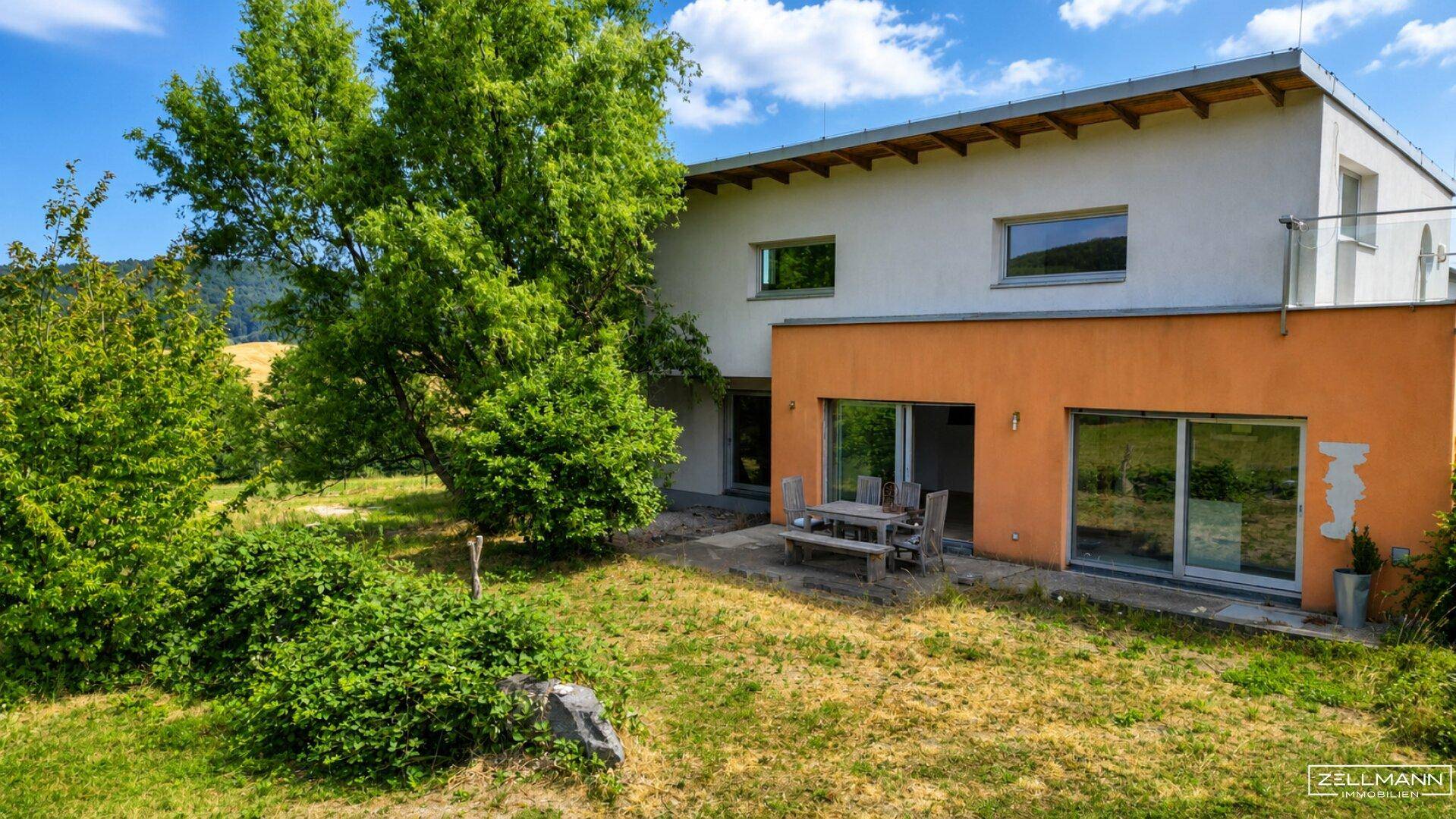 Das moderne Einfamilienhaus mit Terrasse und Garten, umgeben von viel Grün und Bäumen.