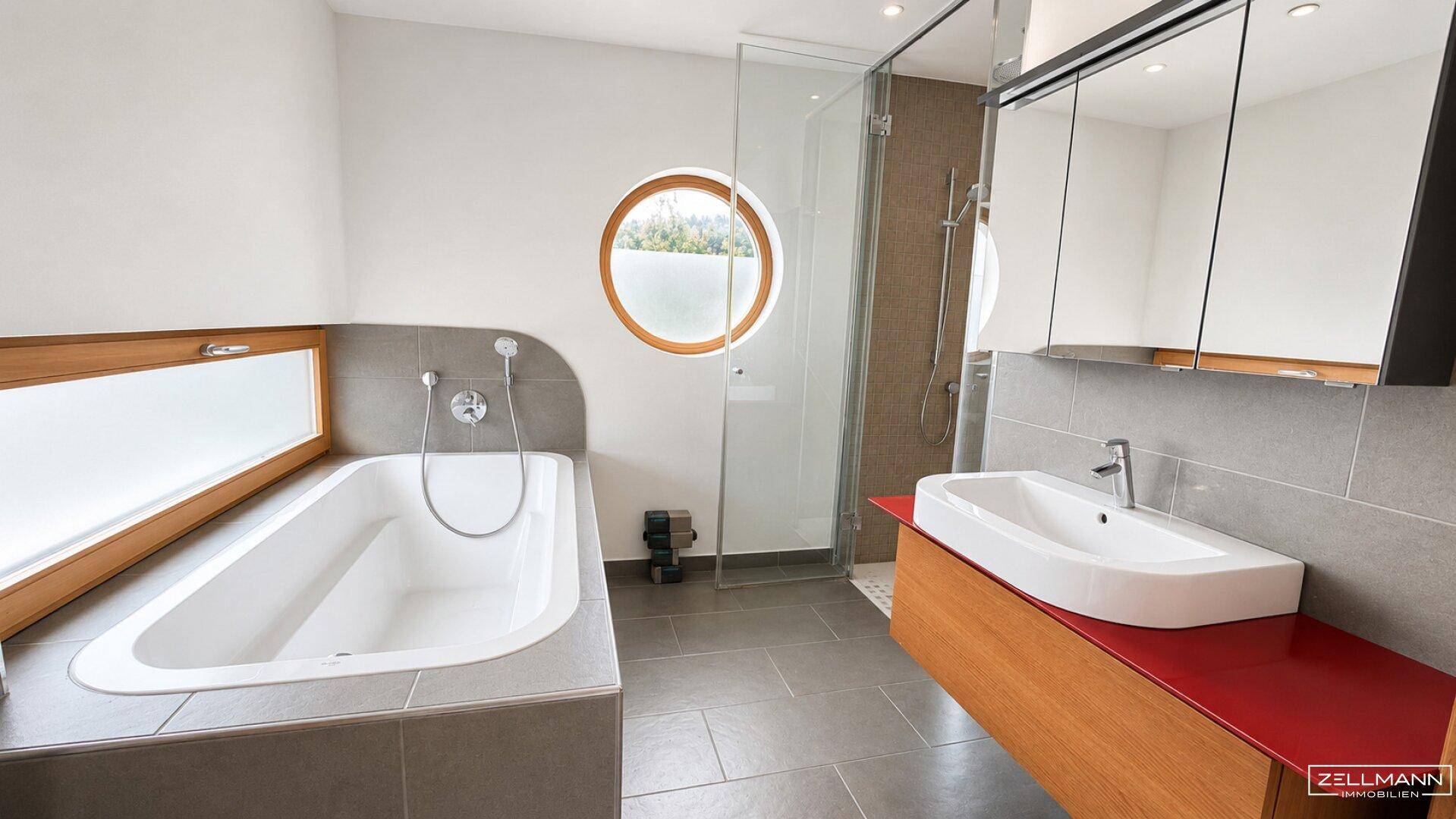 Modernes Badezimmer mit Badewanne, begehbarer Dusche, Doppelwaschbecken und runden Fenstern.