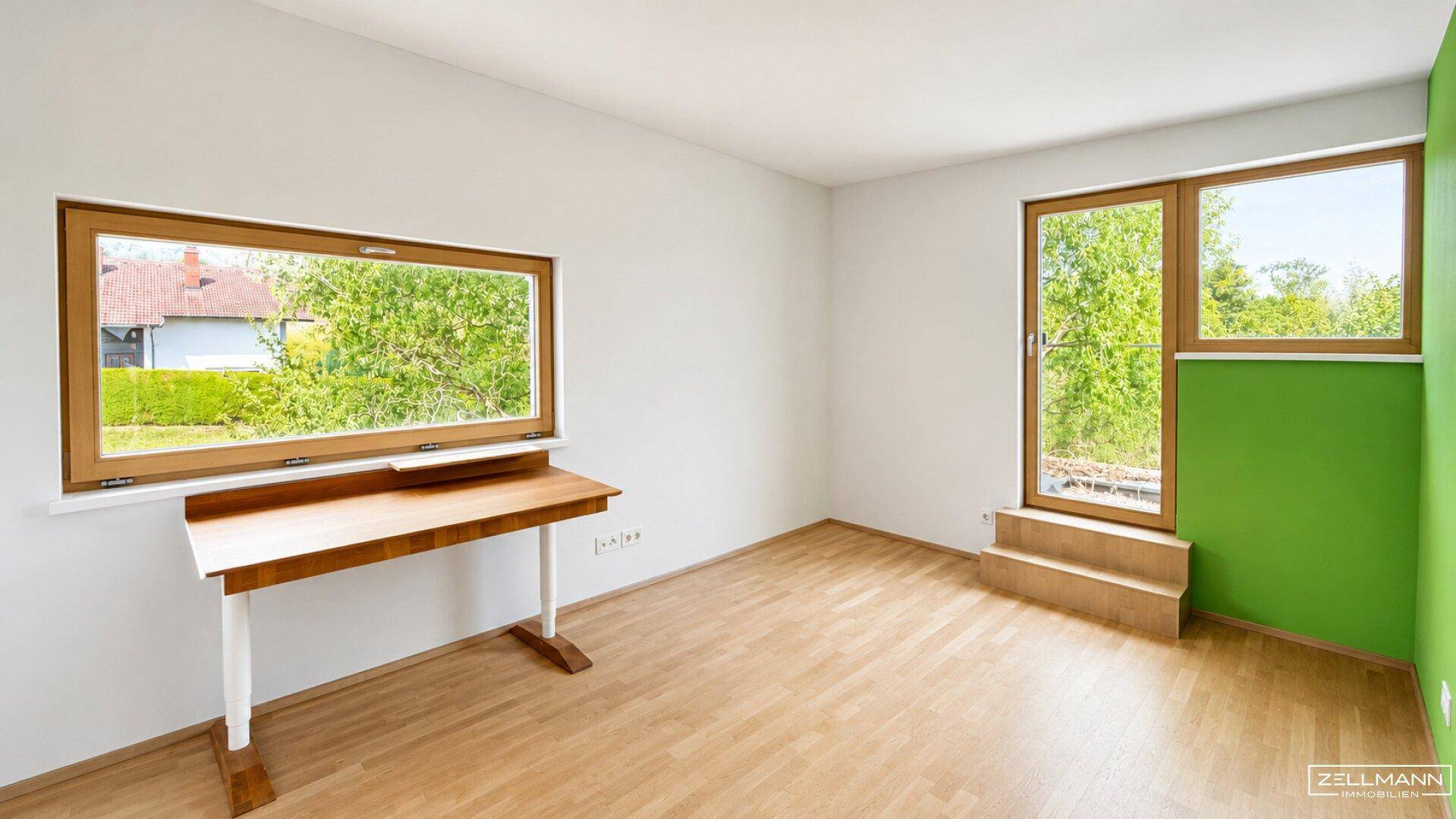 Helles Zimmer mit Parkettboden, großen Fenstern und einer farbigen Akzentwand in Grün.