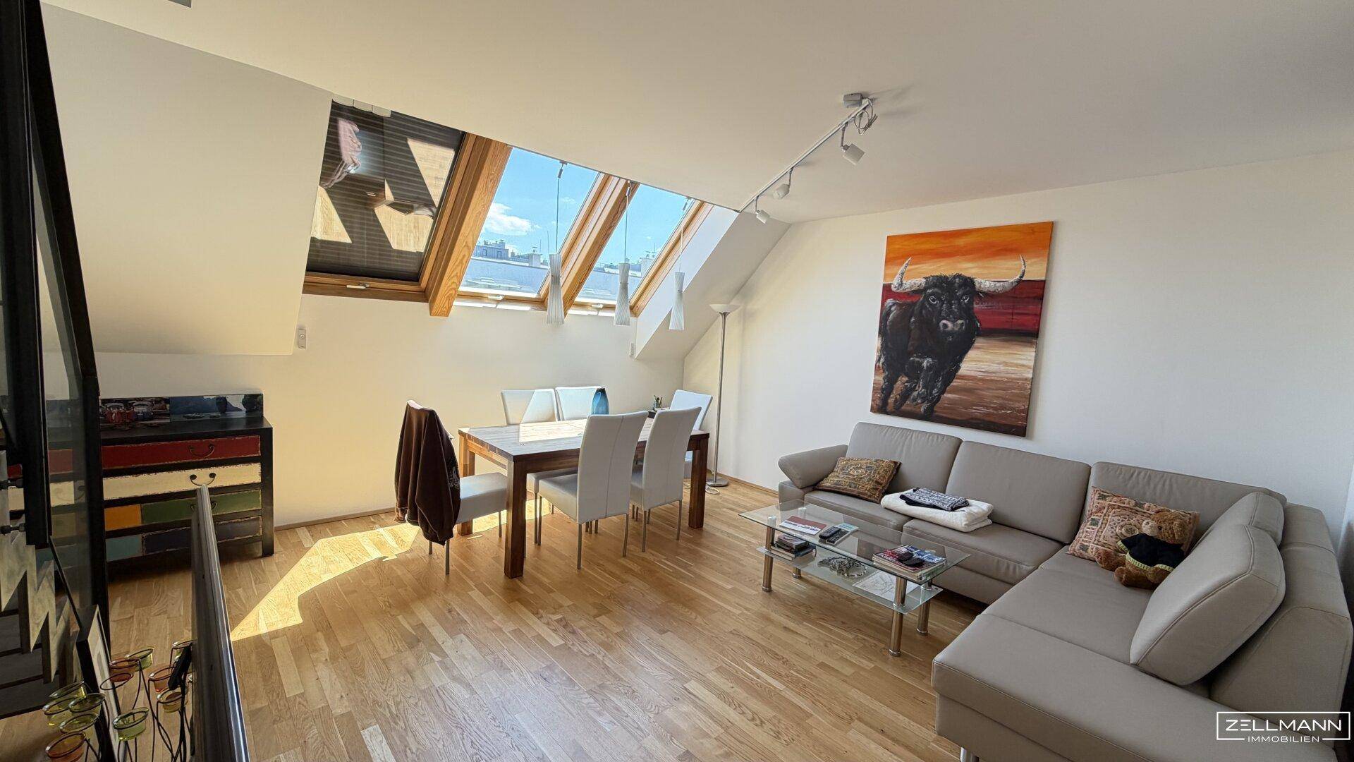 Heller Wohn- und Essbereich im Dachgeschoss mit großen Dachfenstern und Holzboden.