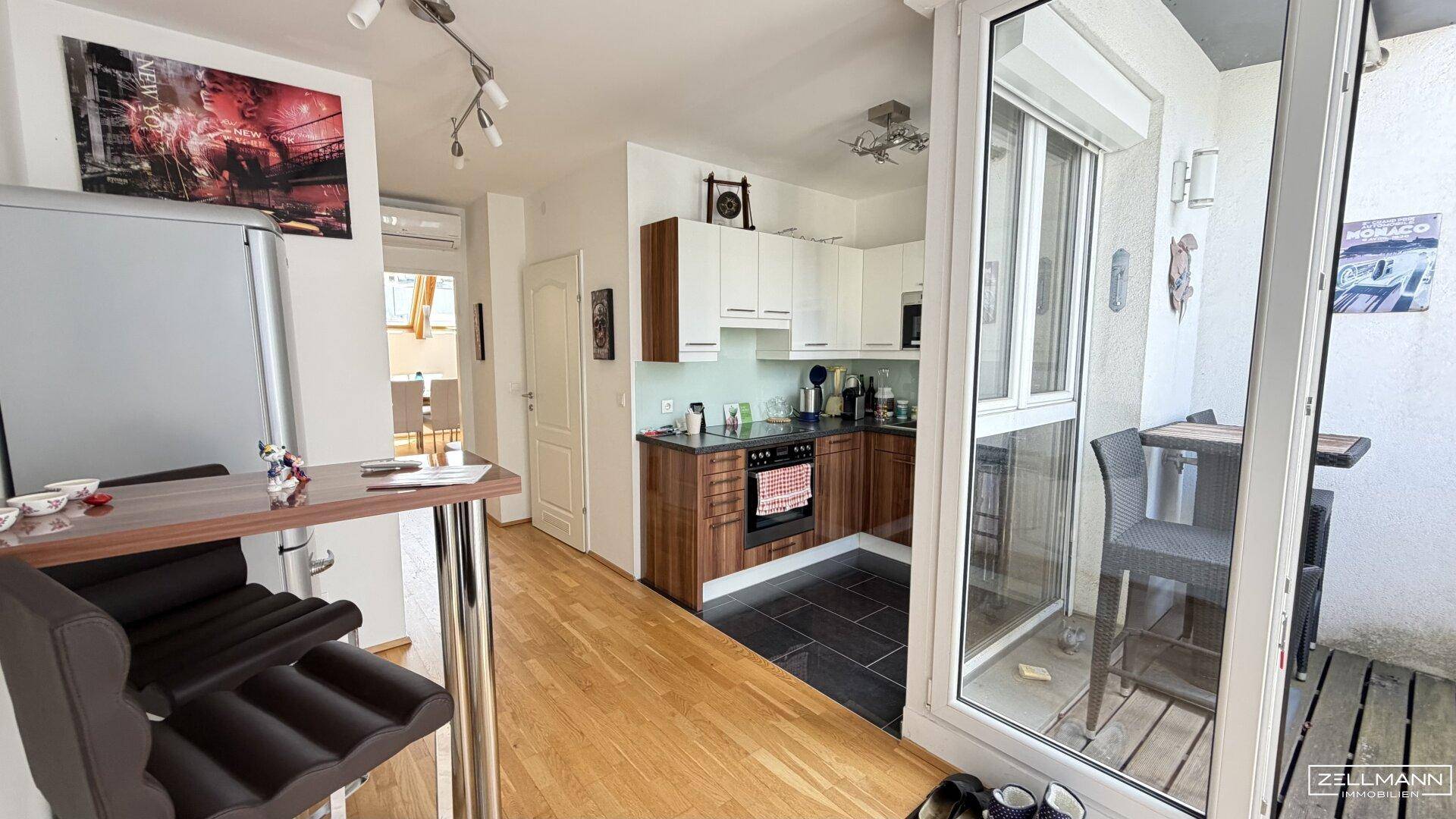 Kompakte Küche mit Holzakzenten und Zugang zu einem kleinen Balkon mit Barhockern.