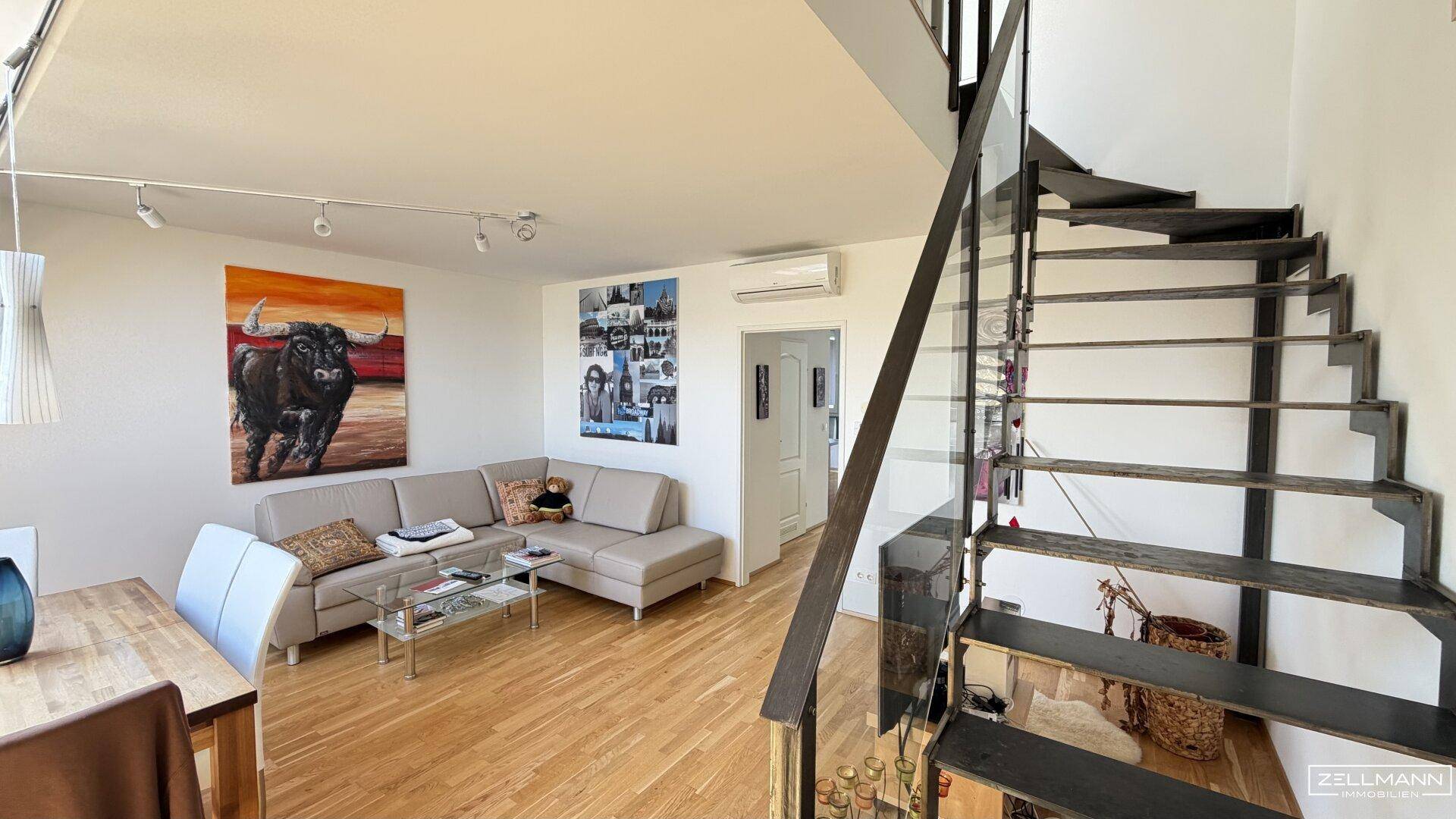 Offener Wohnbereich mit moderner Treppe und gemütlicher Sitzecke unter einem Kunstwerk.