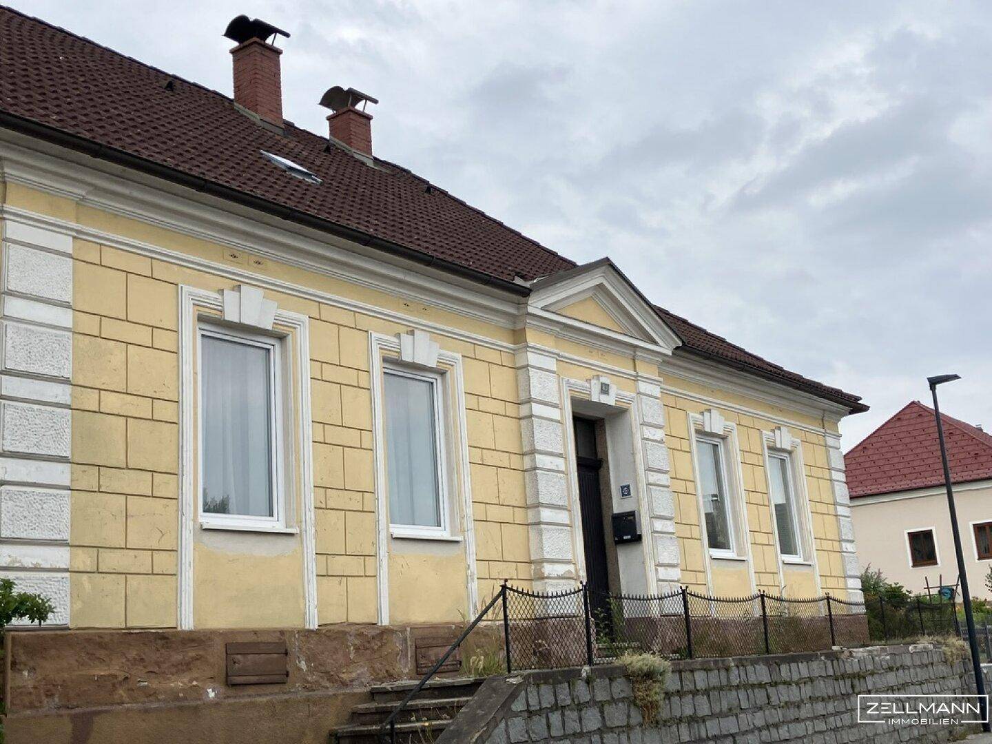 Detailansicht der gelben Fassade eines älteren Gebäudes mit verzierten Fenstern und Eingangsbereich.
