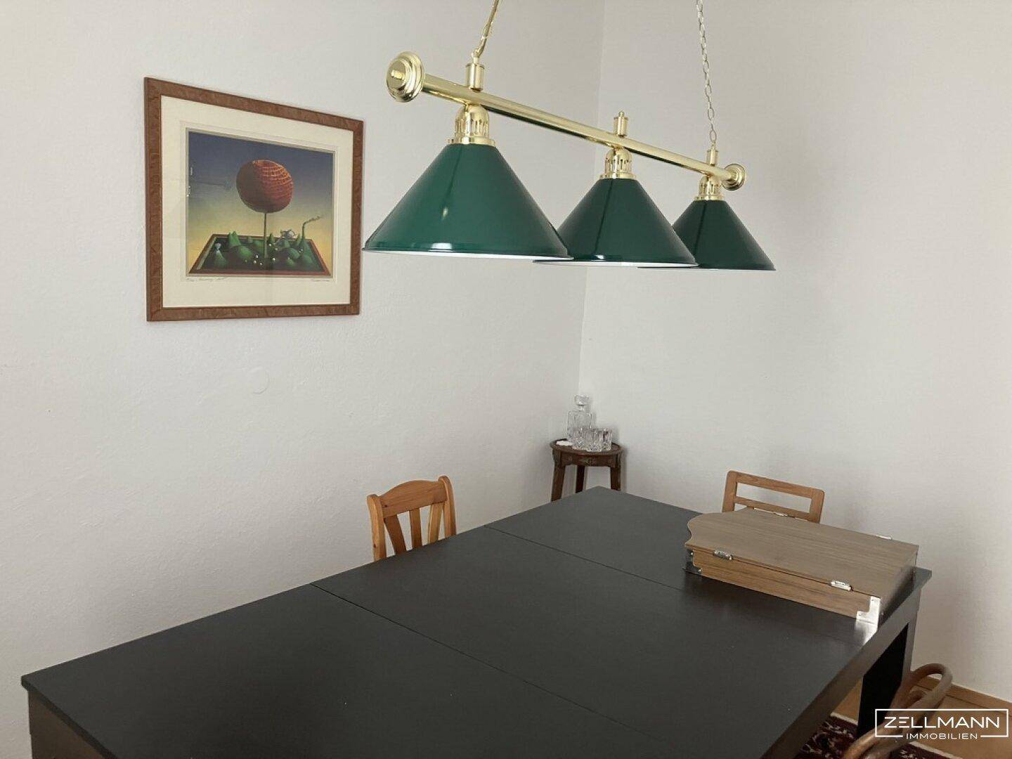Esszimmer mit dunklem Holztisch, grünen Hängelampen und einem gerahmten Bild an der Wand.