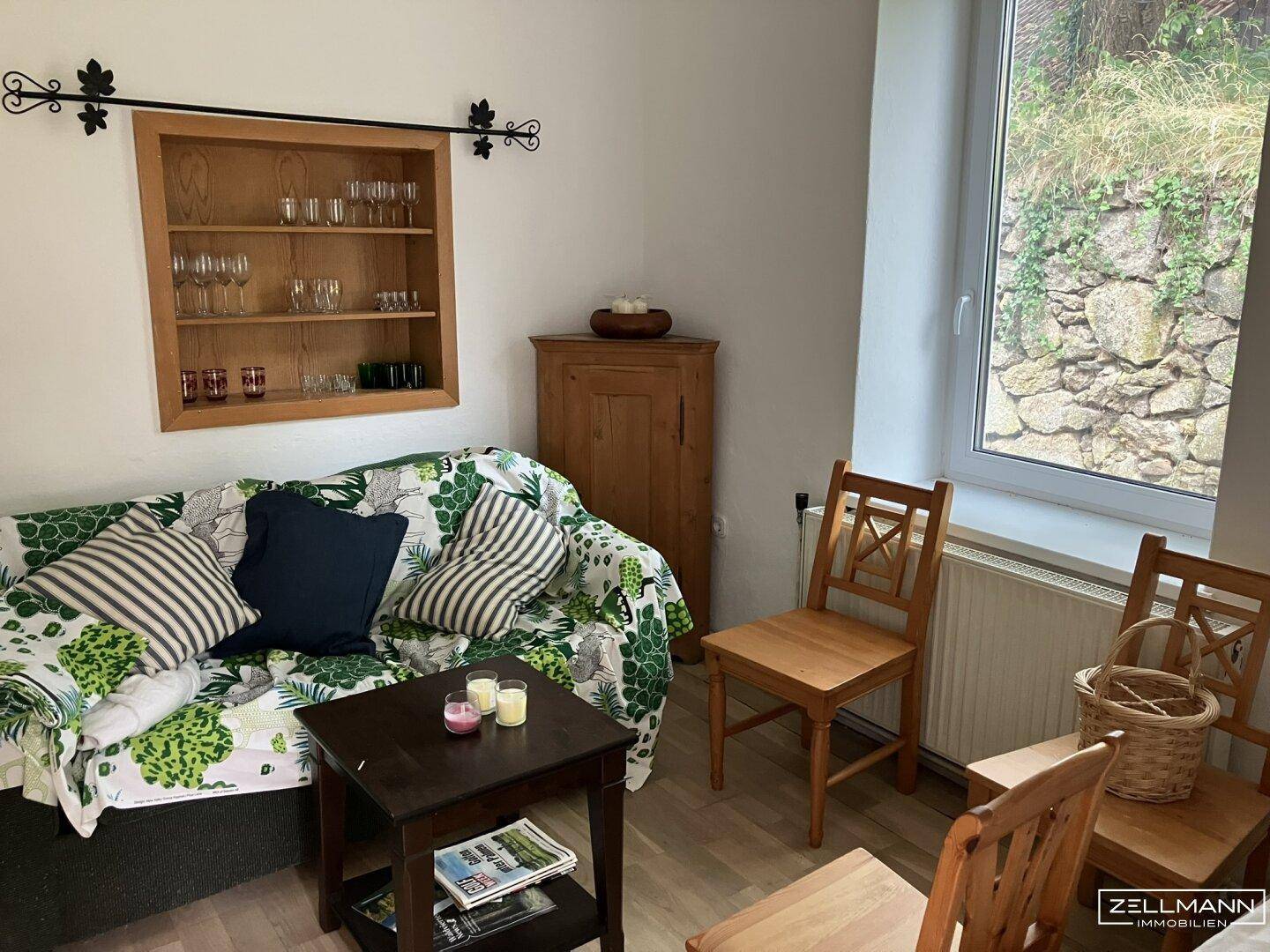 Helles Wohnzimmer mit Sofa, Holzboden und Blick auf eine begrünte Steinmauer im Freien.