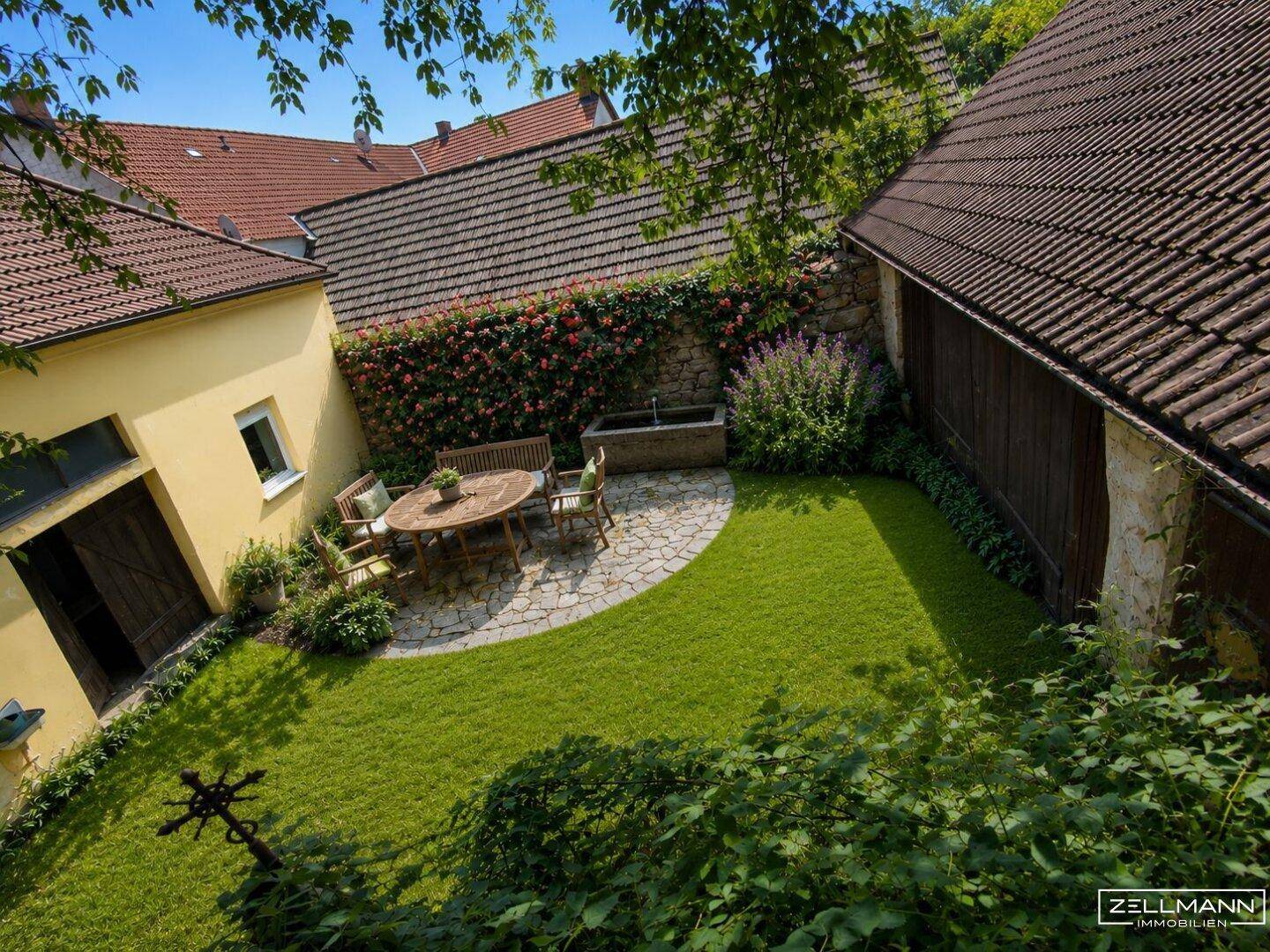 Gepflegter Garten mit Rasenfläche, gepflastertem Sitzbereich und blühenden Pflanzen.
