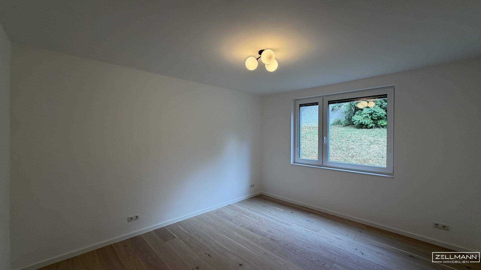 Helles Zimmer mit Holzboden und Fenster mit Blick auf eine grüne Fläche.