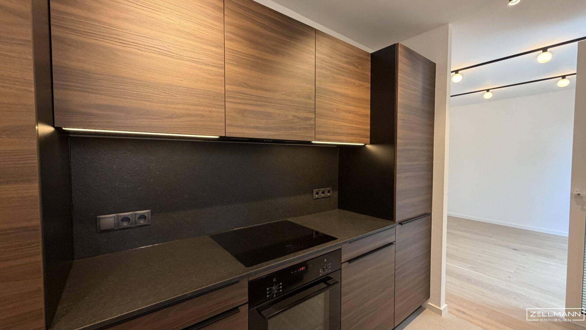 Moderne Einbauküche mit dunklen Holzfronten, integriertem Kochfeld und Backofen.
