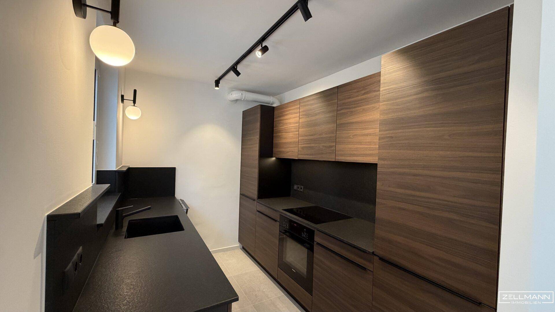 Moderne Küche mit dunklen Holzfronten, integrierten Geräten und schwarzer Arbeitsplatte.