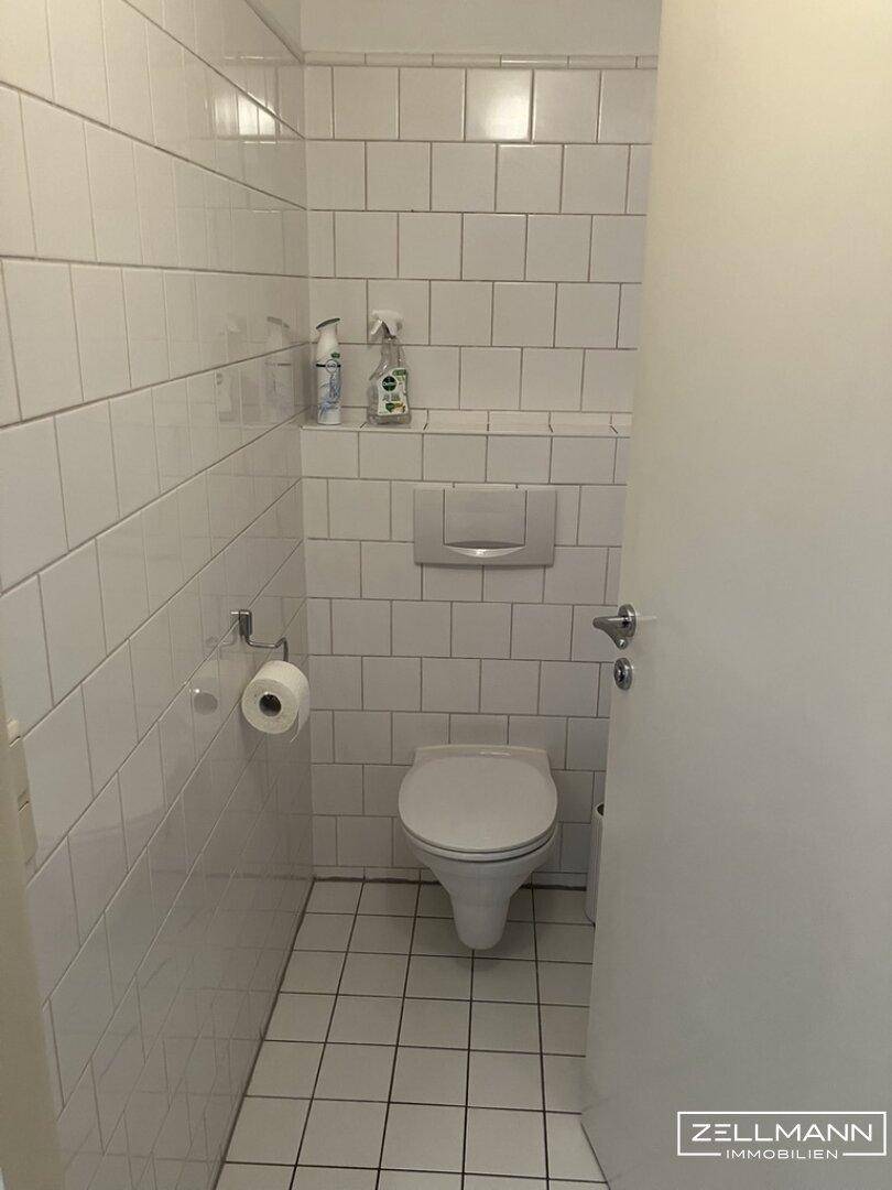 Kleines, weiß gefliestes Gäste-WC mit wandhängender Toilette und Fliesenboden.