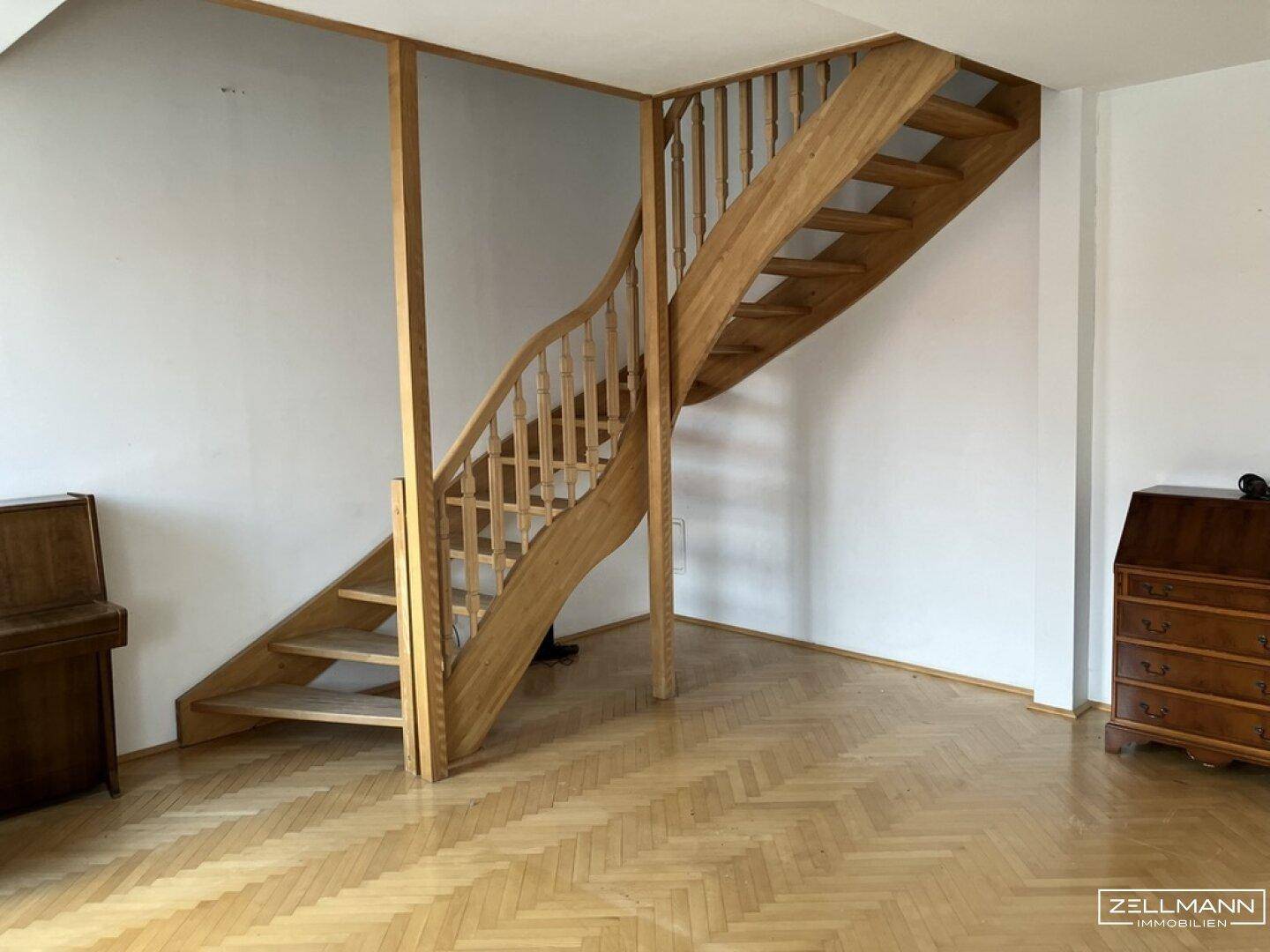 Holztreppe mit geschwungenem Geländer in einem hellen Wohnbereich mit Parkettboden.