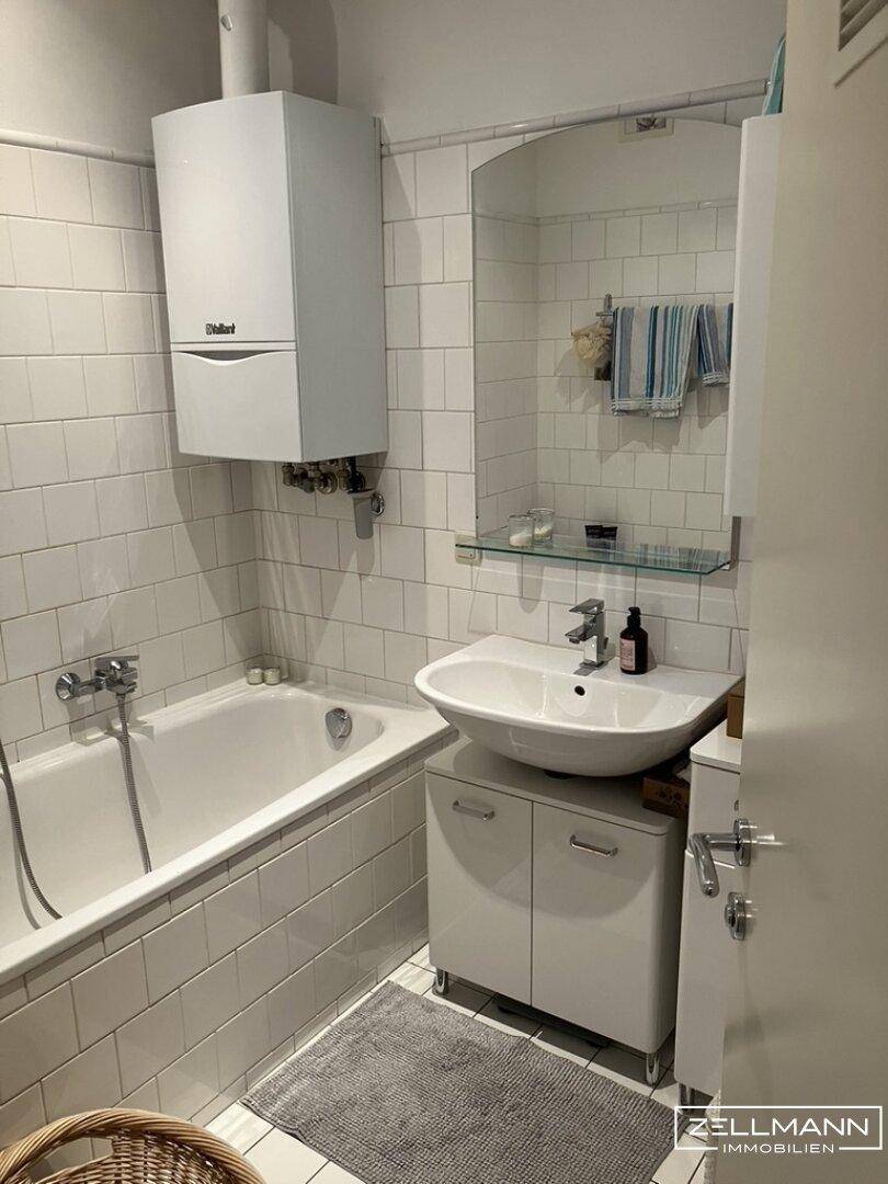 Gefliestes Badezimmer mit Badewanne, Waschbecken und Gastherme an der Wand.