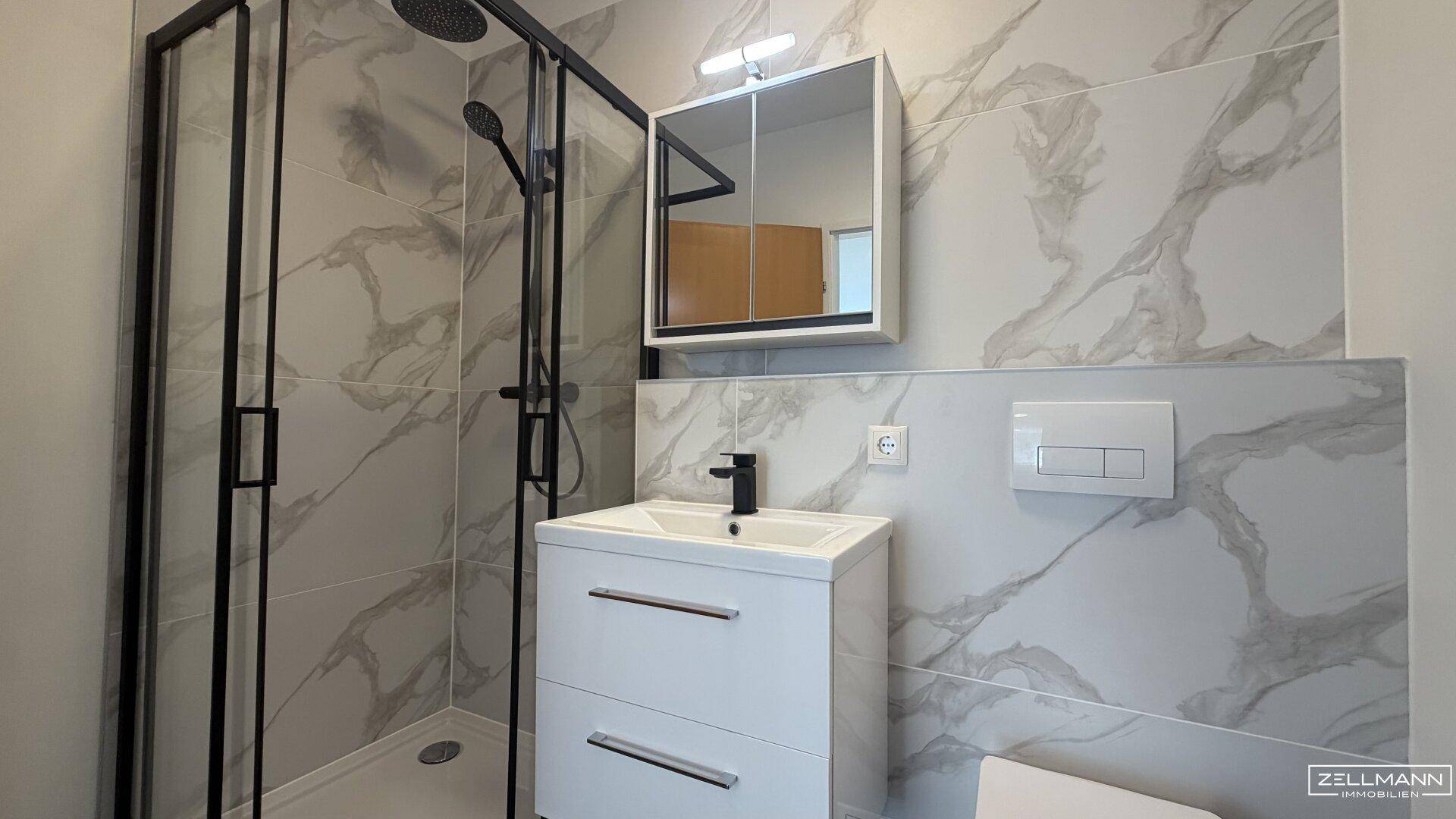 Modernes Badezimmer mit Duschkabine, Waschtisch und eleganten Fliesen in Marmoroptik.