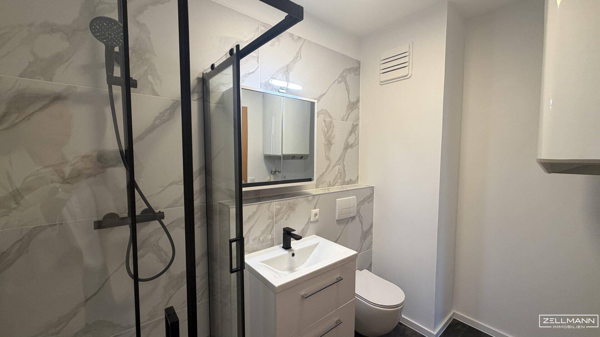 Modernes Badezimmer mit Duschkabine, Waschtisch und eleganten Fliesen in Marmoroptik.