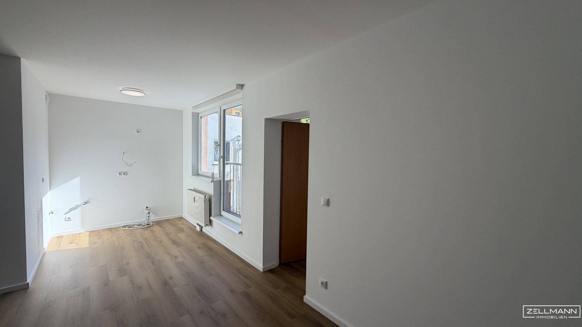 Geräumiger Wohnbereich mit Holzboden, hellen Wänden und Zugang zu einem Balkon.