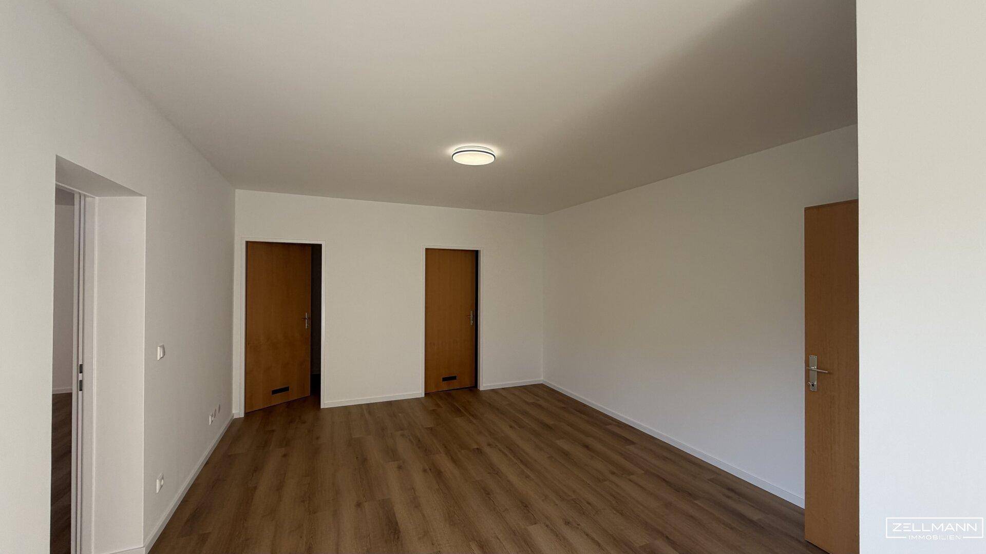 Geräumiger Raum mit Holzboden und mehreren Türen, ideal als Wohn- oder Essbereich.