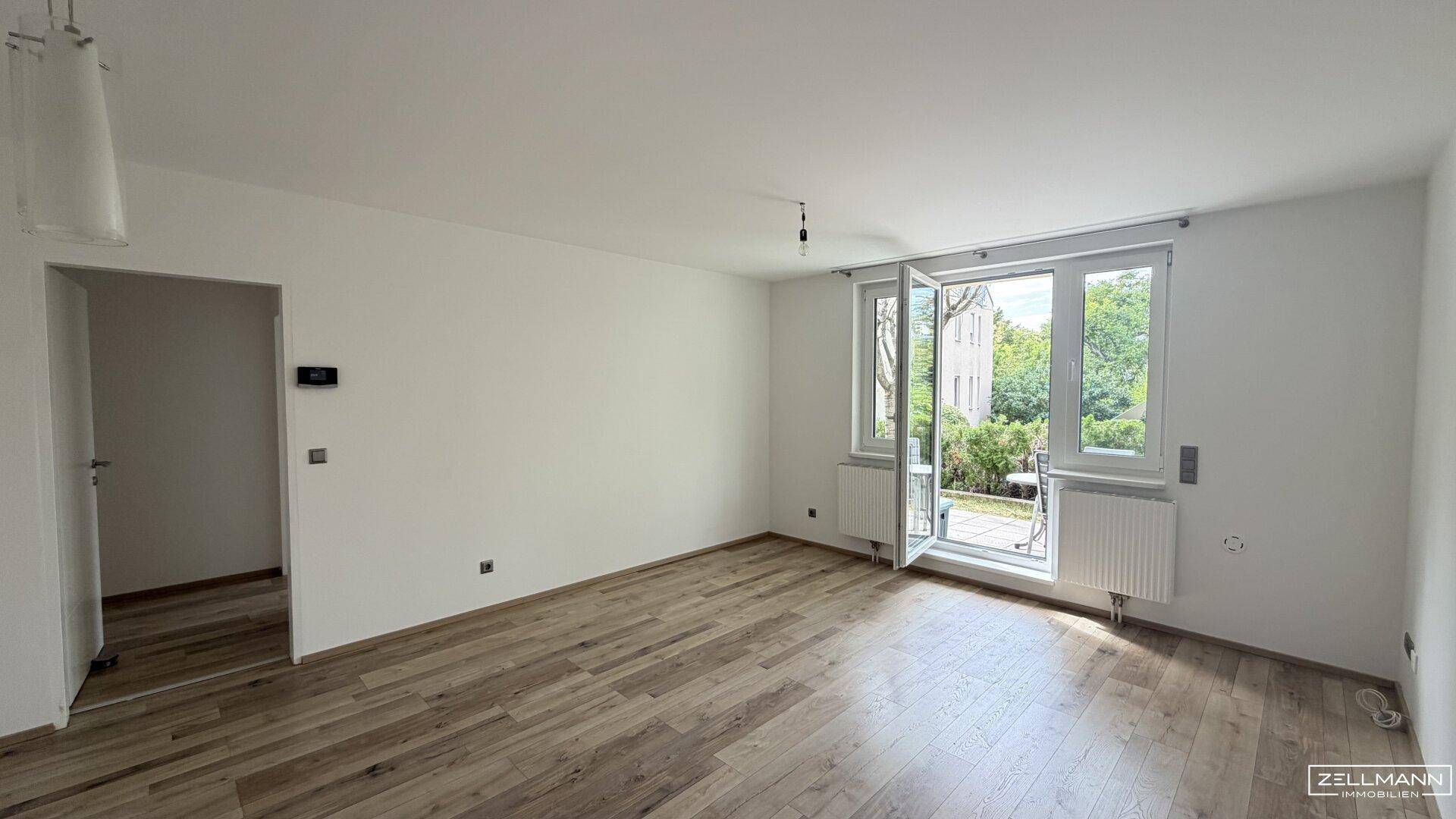 Helles Wohnzimmer mit Holzboden und Zugang zu einem Außenbereich, ideal für Entspannung.