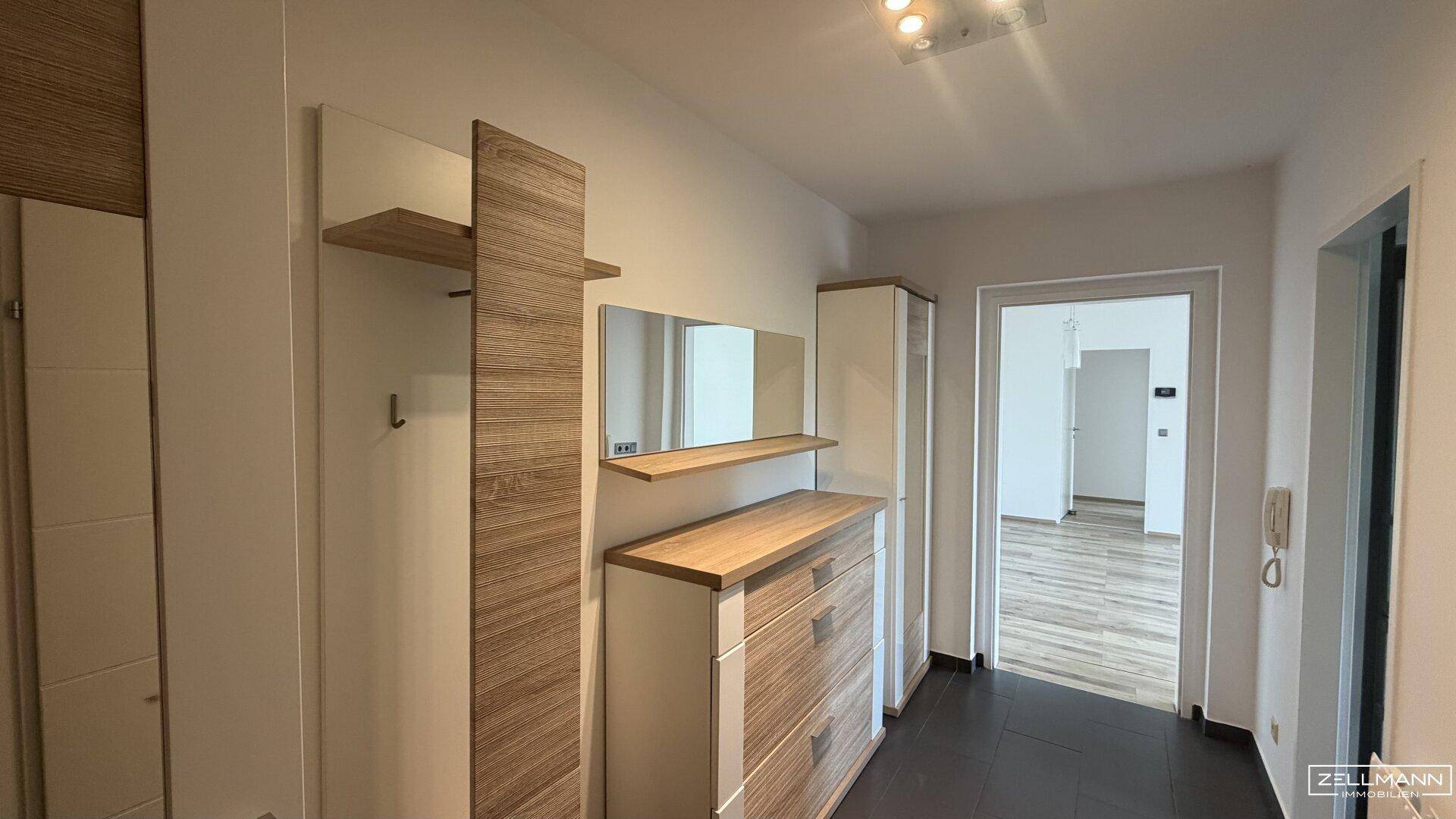 Heller Flur mit Holzmöbeln und Spiegel, der zu weiteren Räumen führt.