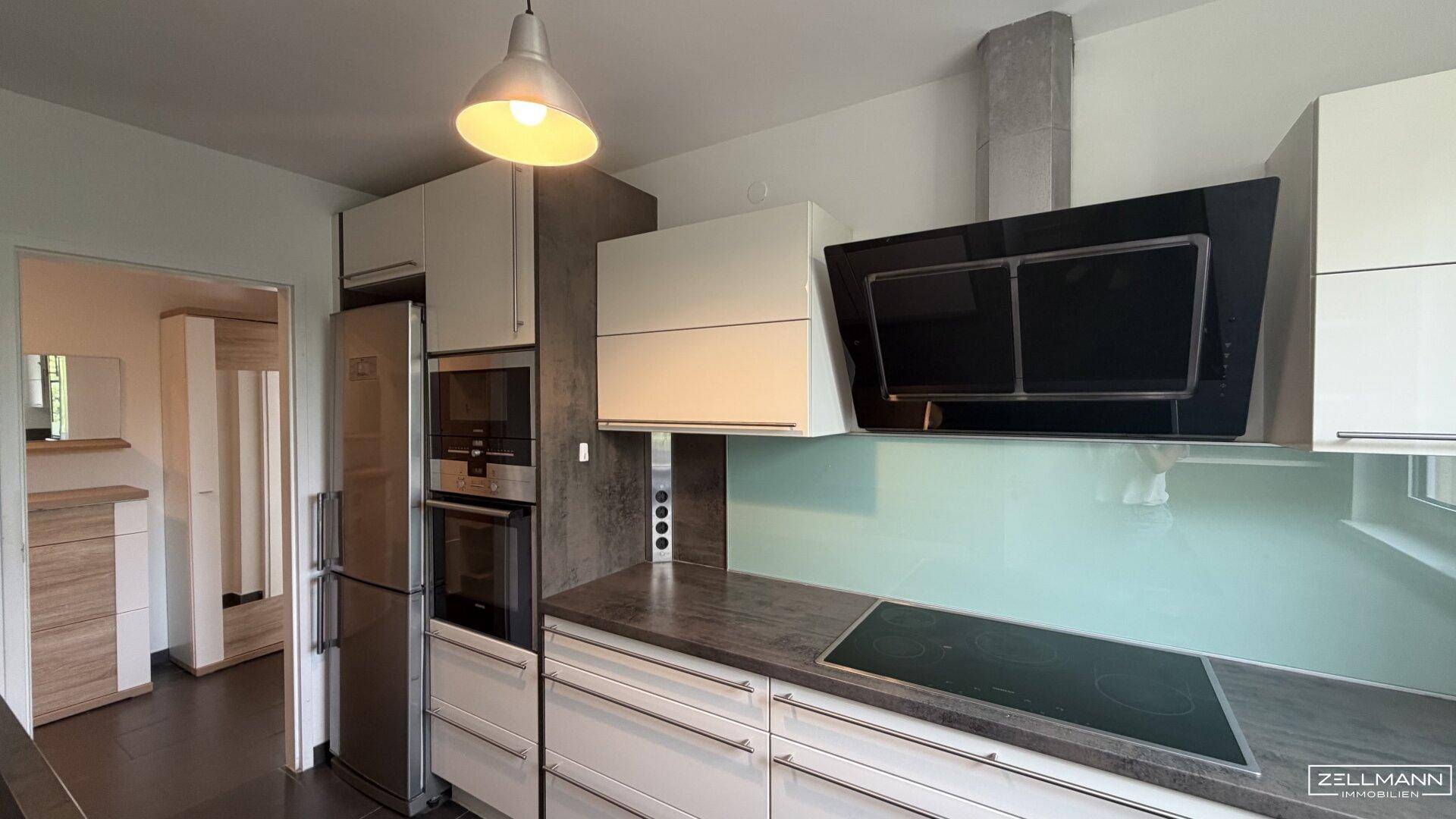 Moderne Küche mit Einbaugeräten, Induktionskochfeld und Dunstabzugshaube in hellem Design.