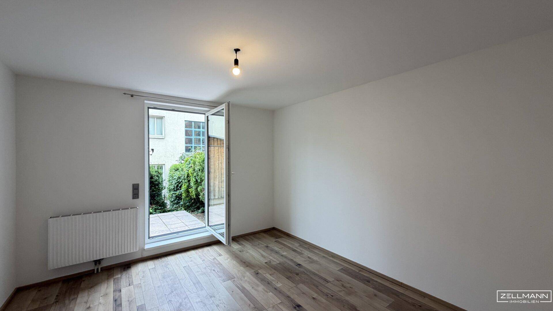Helles Schlafzimmer mit Holzboden und Fenster, das den Blick ins Grüne freigibt.