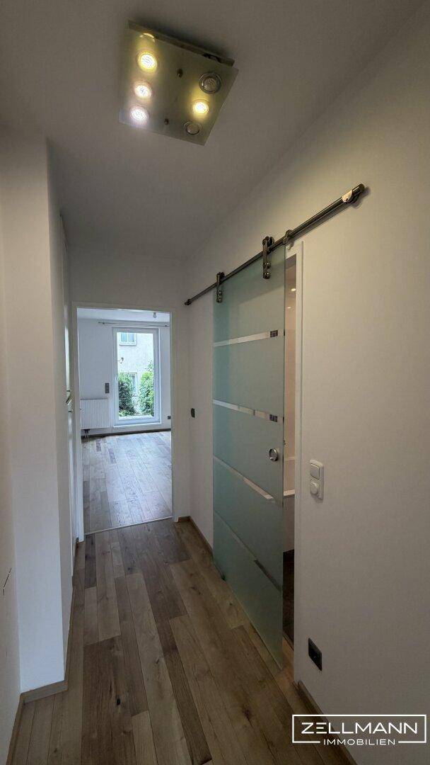 Heller Flur mit Schiebetür aus Glas und Holzboden, der zu weiteren Räumen führt.