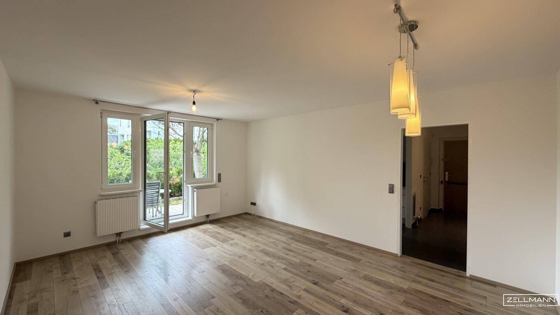 Geräumiges Wohnzimmer mit Holzboden und Zugang zu einem sonnigen Außenbereich.
