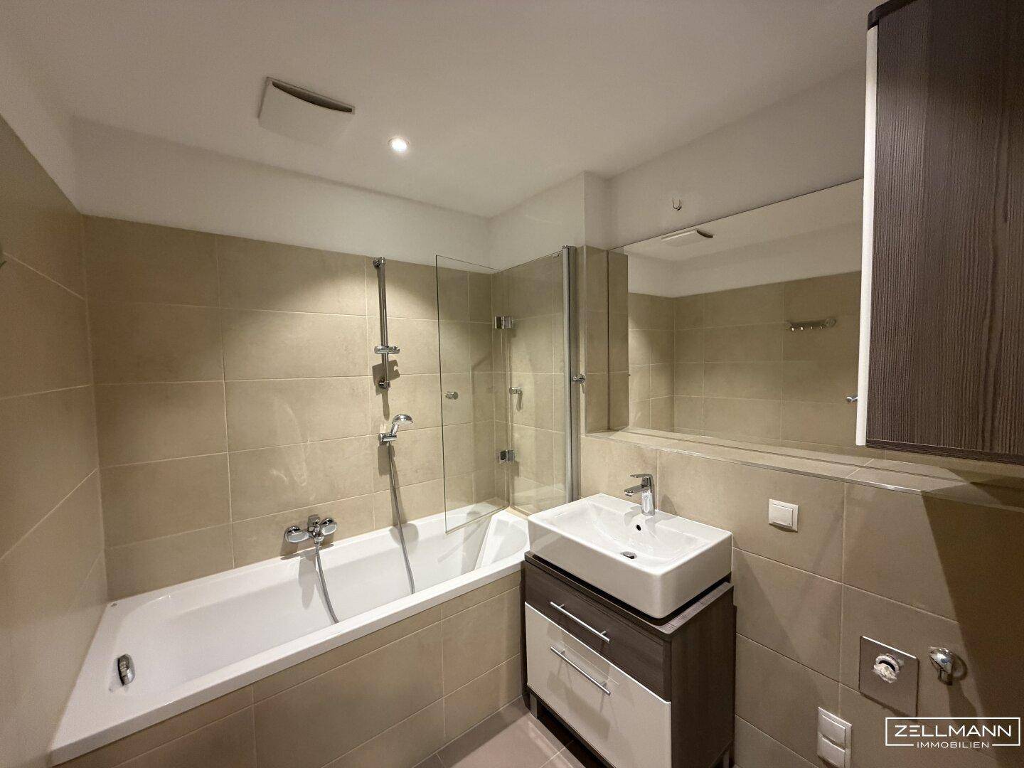 Modernes Badezimmer mit Badewanne, integrierter Dusche und beigefarbenen Fliesen.