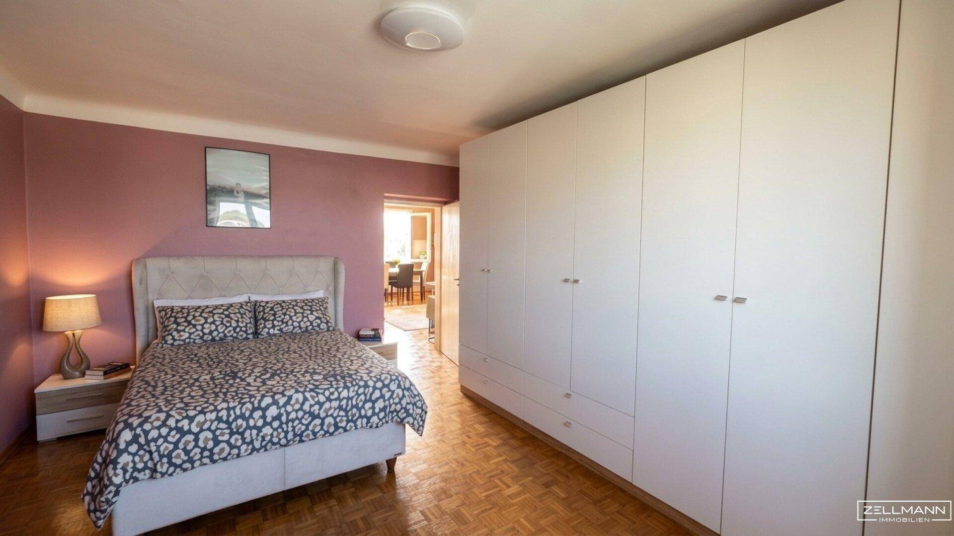 Gemütliches Schlafzimmer mit rosa Wänden, großem Kleiderschrank und Zugang zu einem weiteren Raum.