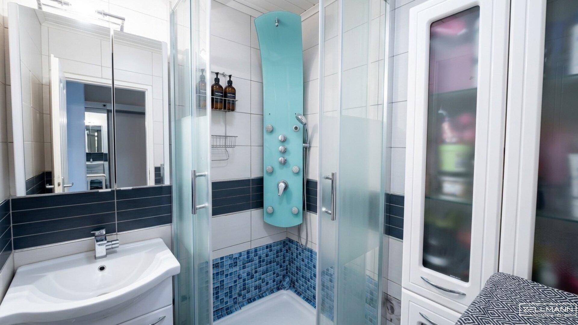 Modernes Badezimmer mit Duschkabine, weiß-blauen Fliesen und integriertem Spiegelschrank.