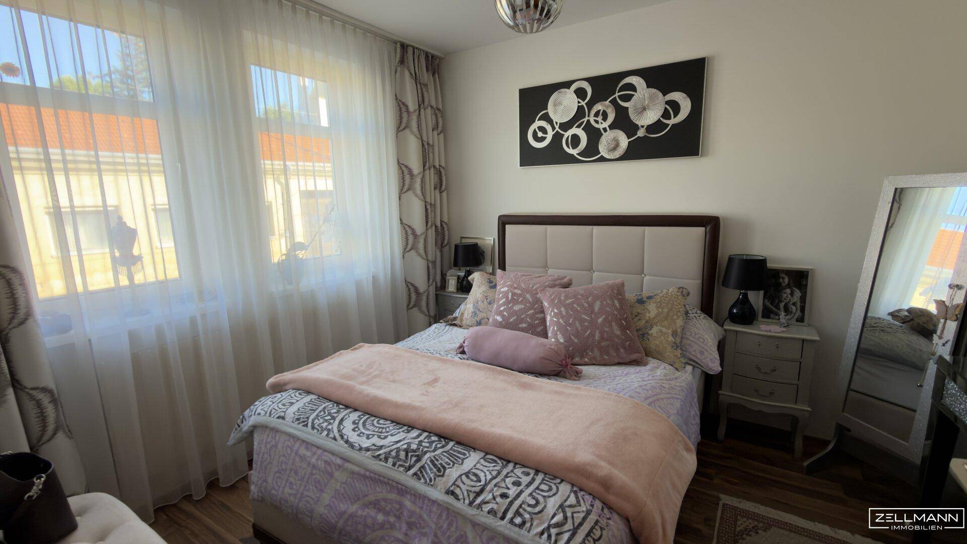 Gemütliches Schlafzimmer mit Doppelbett, Nachttischen und viel Tageslicht durch große Fenster.