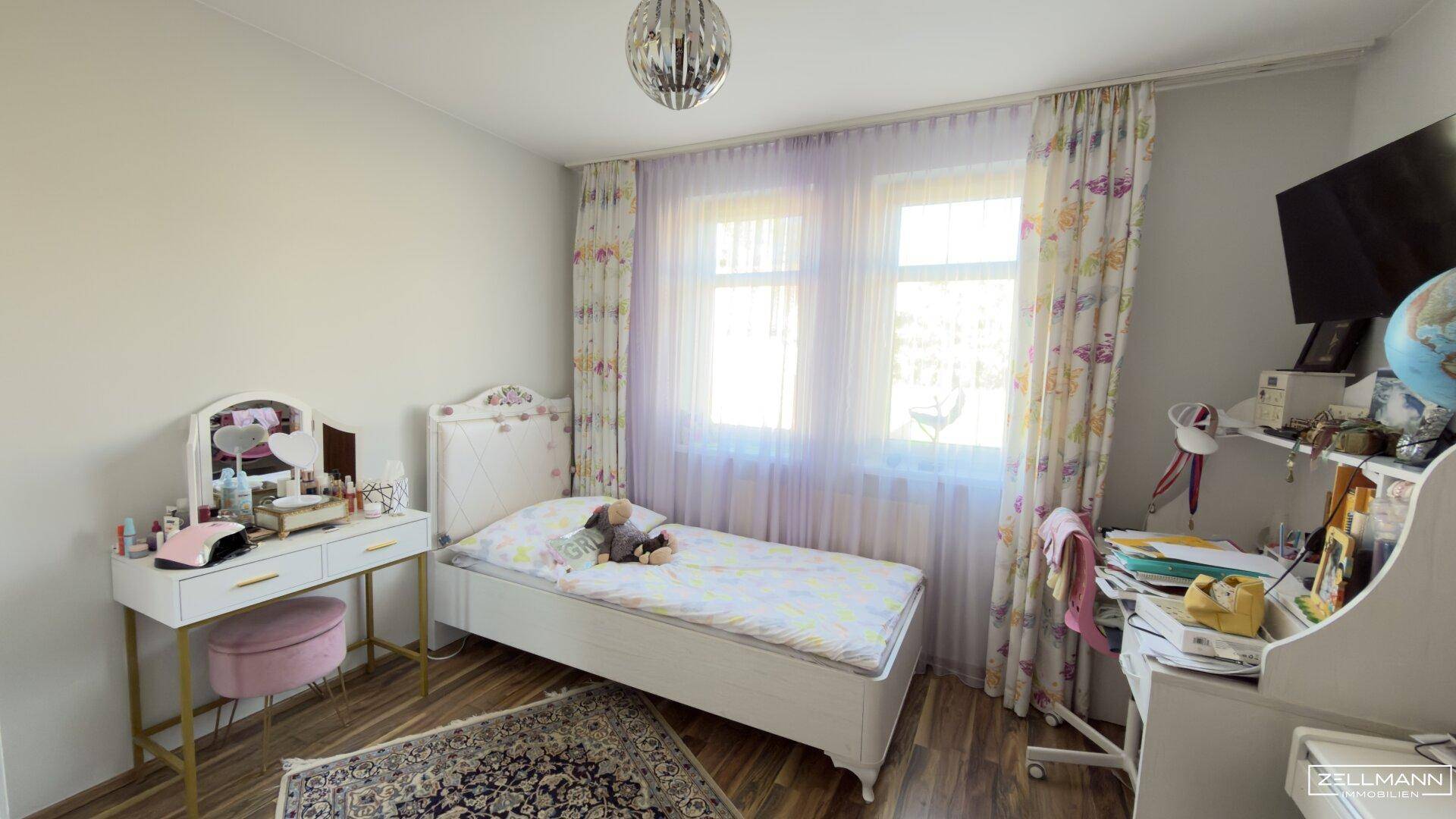 Helles Kinderzimmer mit Einzelbett, Schminktisch und Schreibtisch am Fenster für viel Tageslicht.
