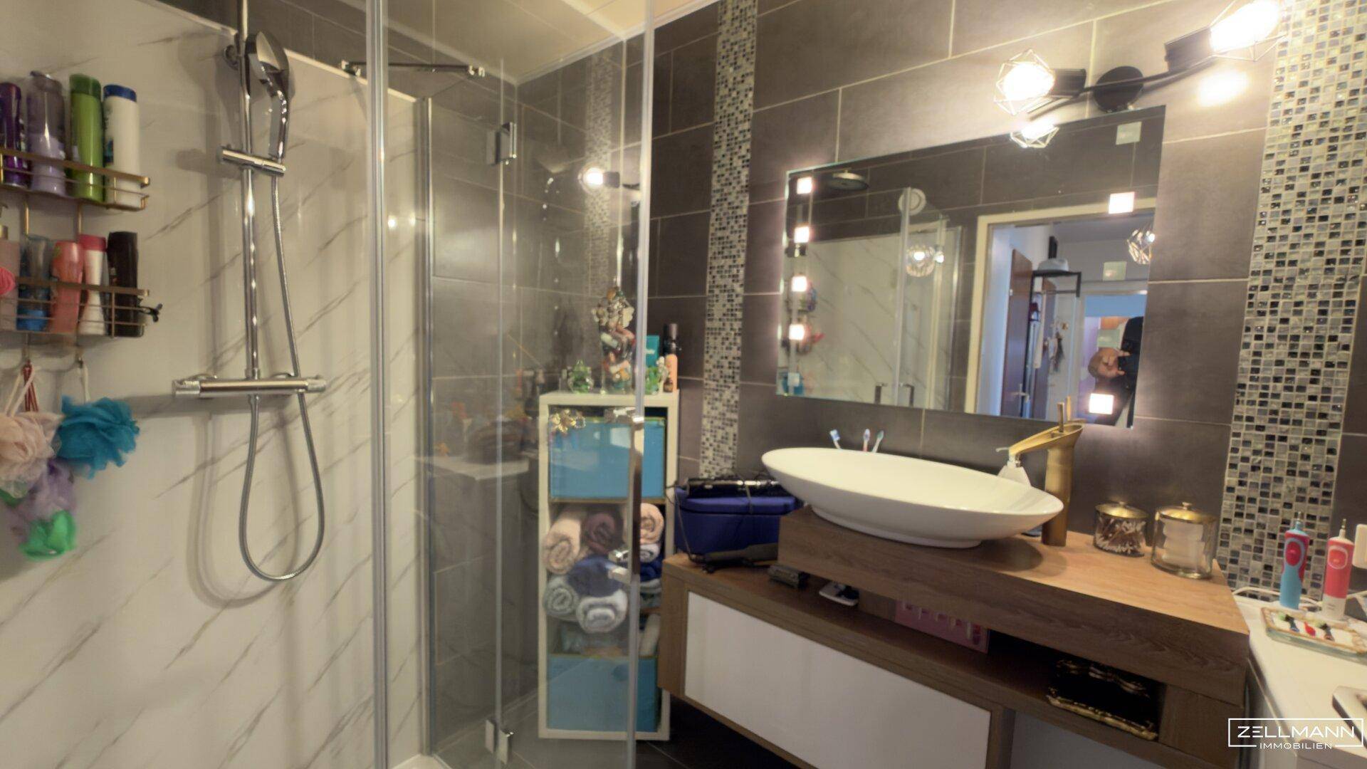 Modernes Badezimmer mit großer Duschkabine, Aufsatzwaschbecken und beleuchtetem Spiegel.