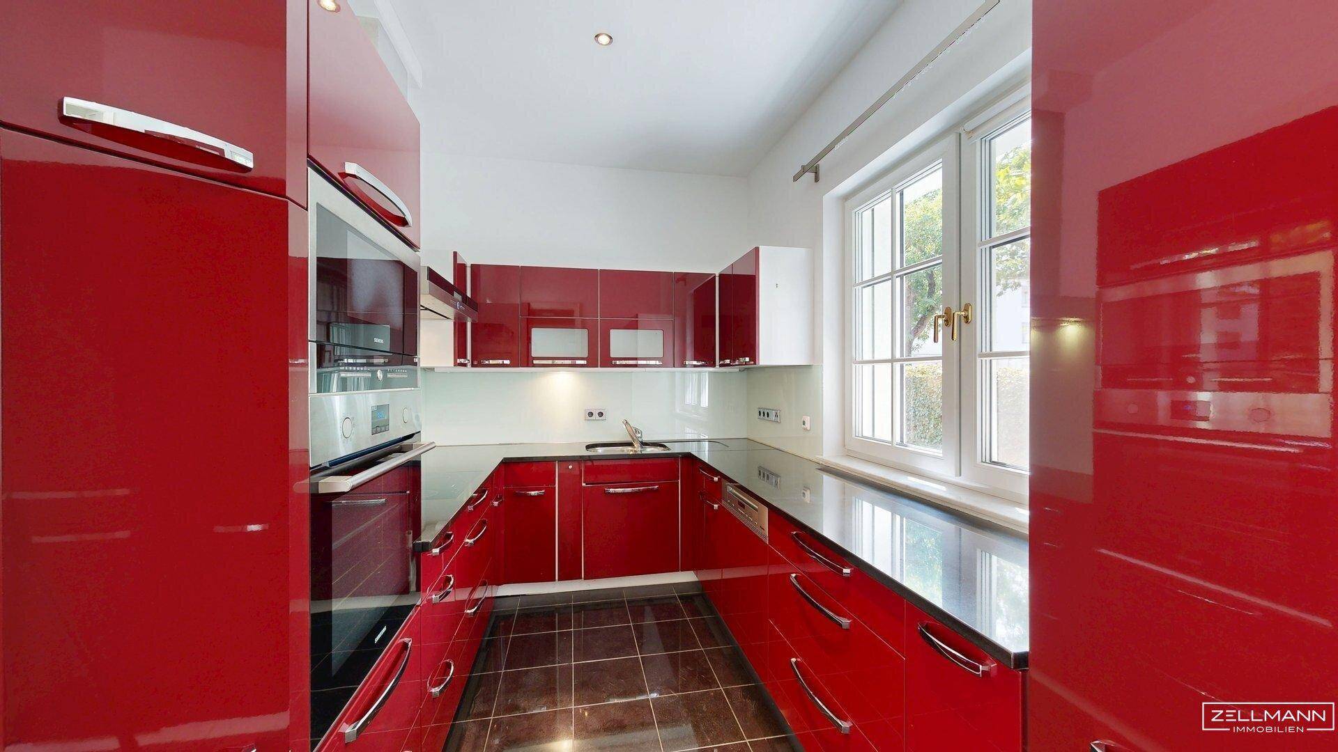Moderne Küche mit glänzenden roten Fronten, Einbaugeräten und Fenster.
