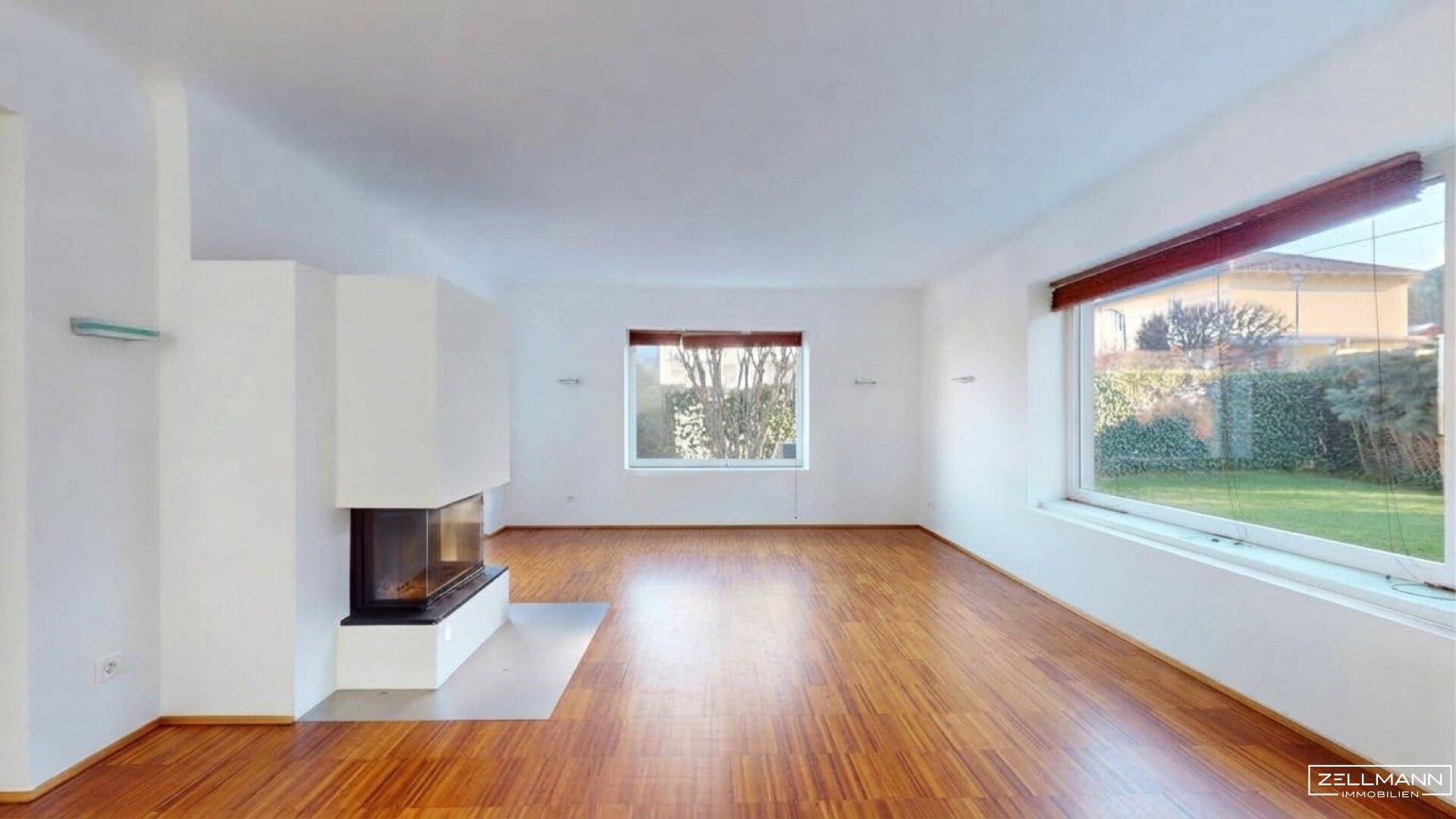Helles Wohnzimmer mit modernem Kamin und Holzboden, Blick in den Garten.